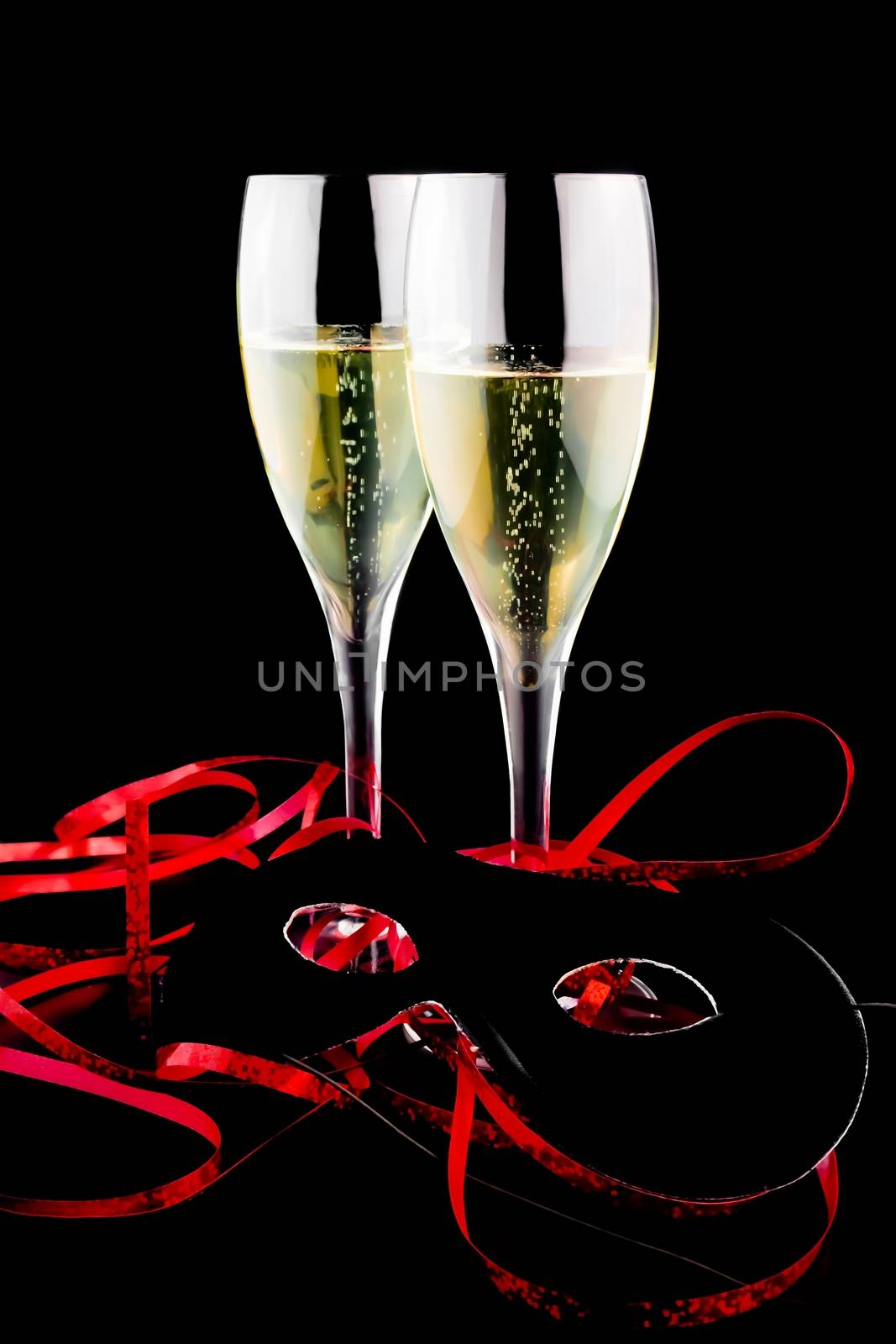 two flutes with champagne near a carnival mask on black background