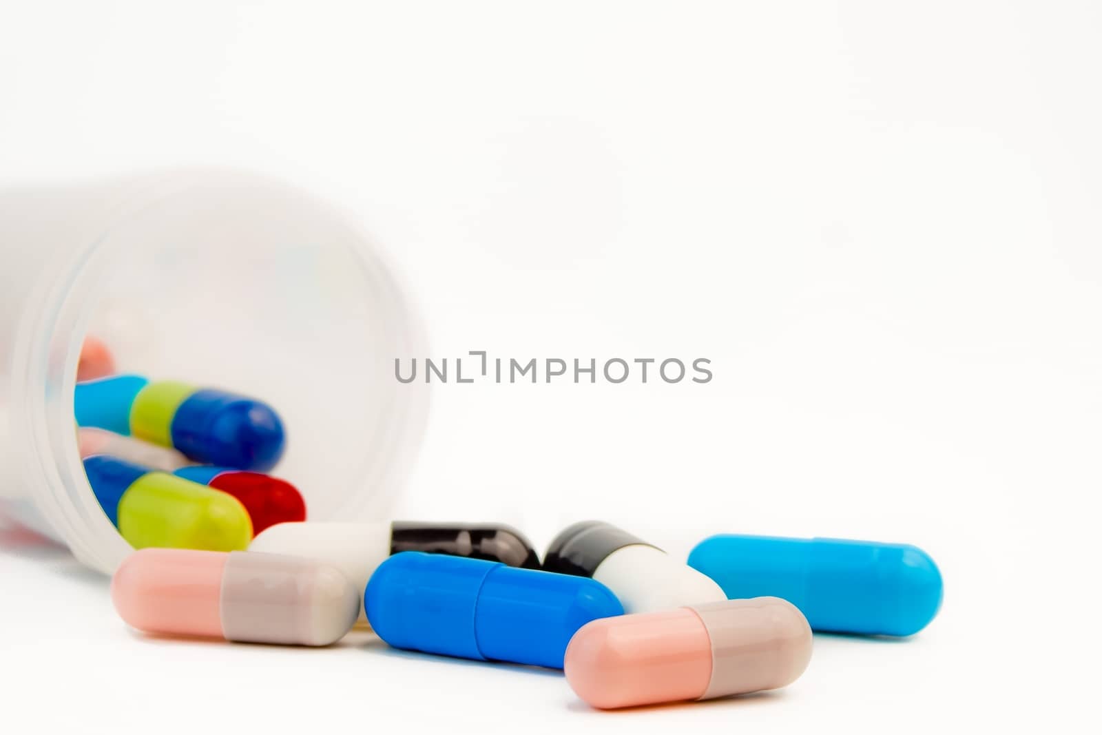 closeup of colored pills with unfocused bottle on white background