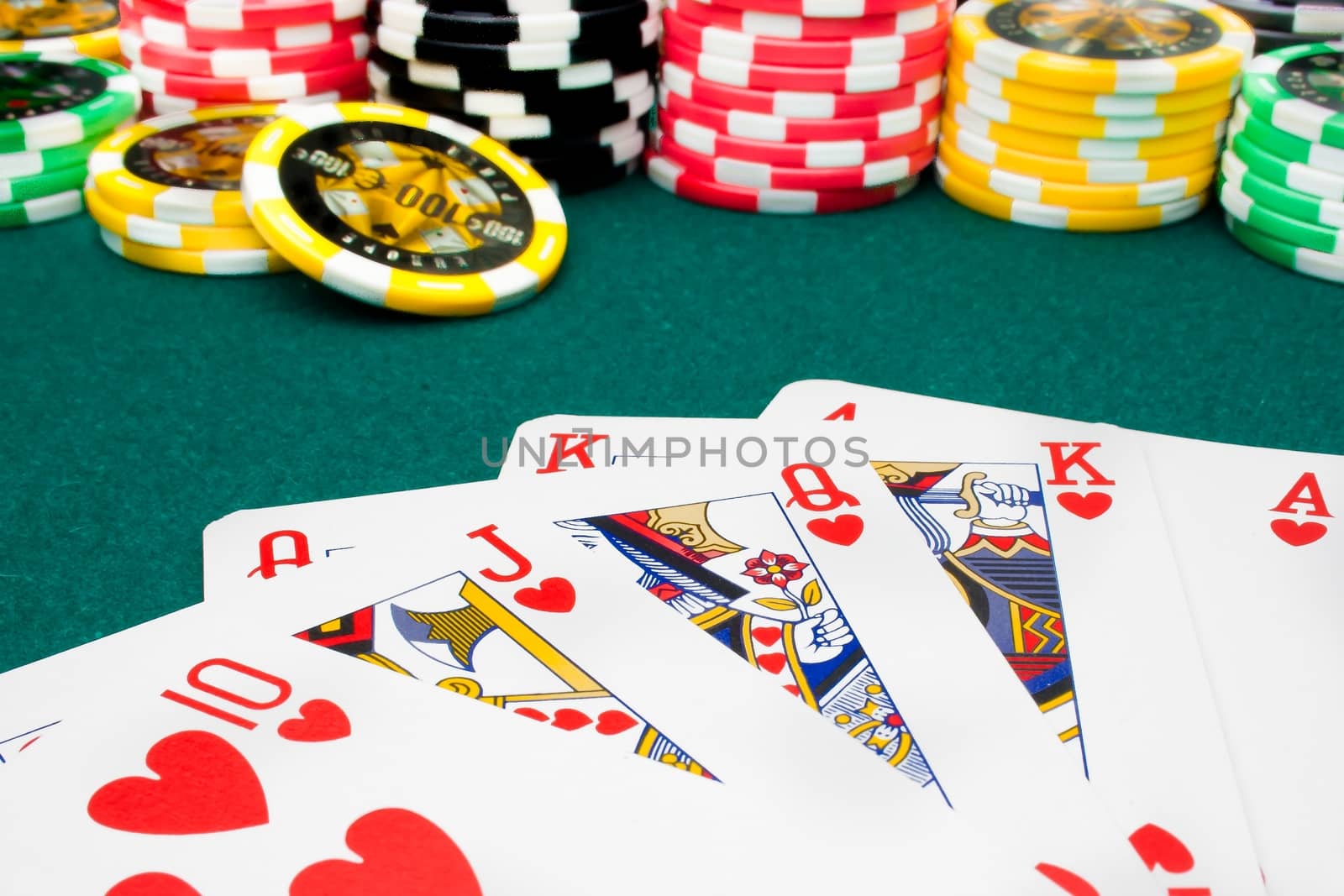  royal flush and unfocused gambling chips of a green fabric background 