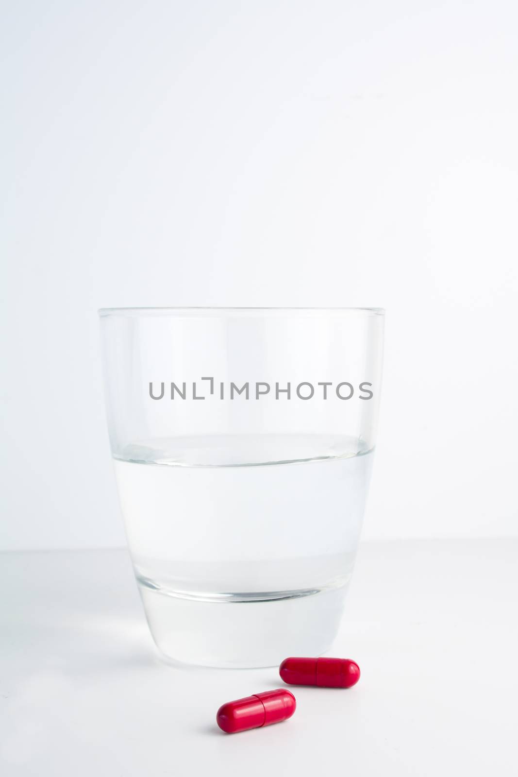 detail of red pills next to a water glass isolated on white background