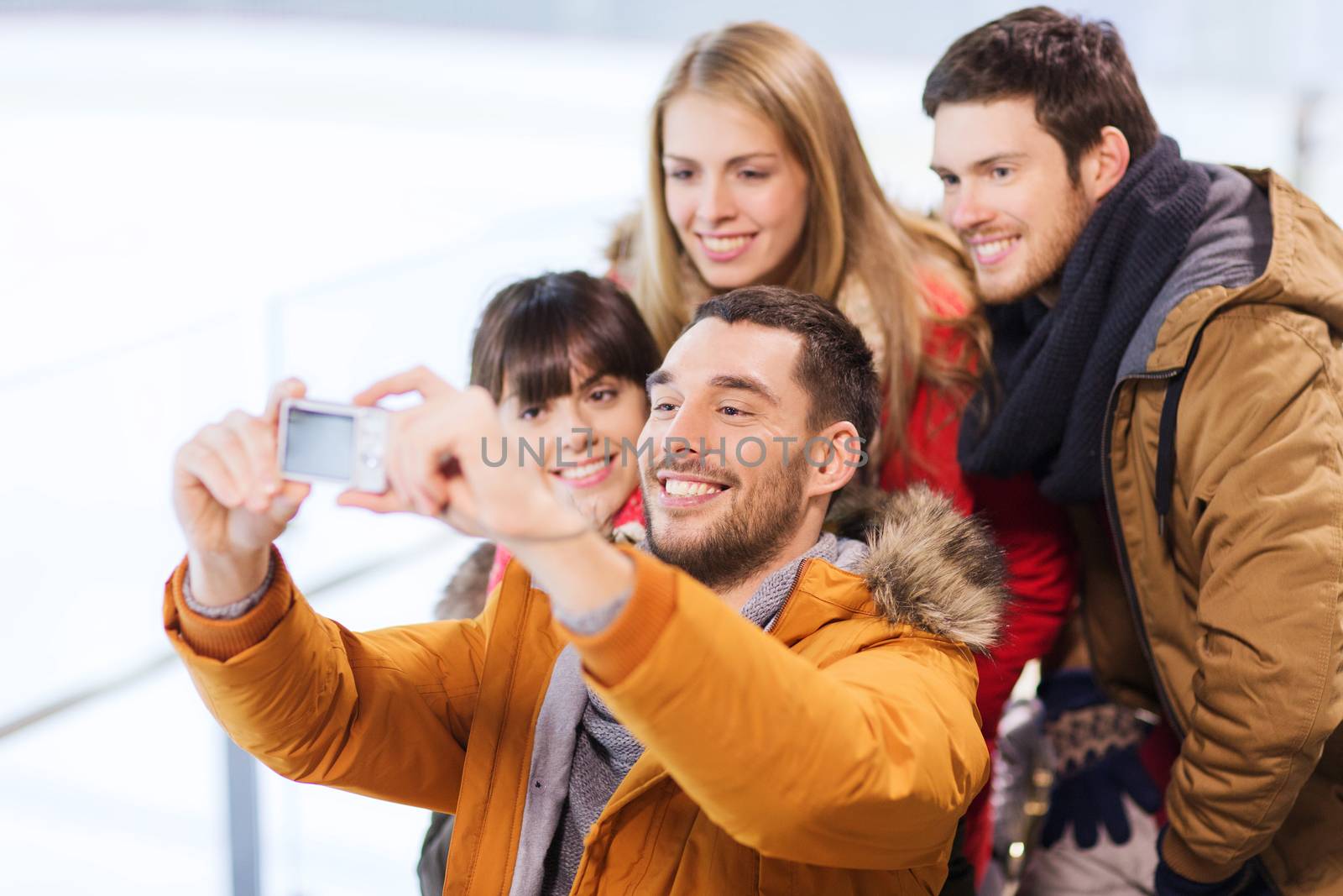 people, friendship, technology and leisure concept - happy friends taking selfie with digital camera on skating rink