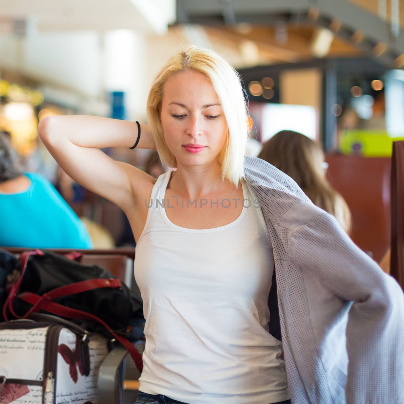 Casual blond young woman feeling cold and putting on her jacket while waiting to board a plane at the departure gates. Air condition on public transport.