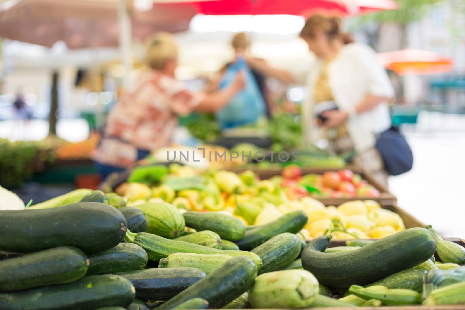 Farmers' food market stall with variety of organic vegetable. Vendor serving and chating with customers.