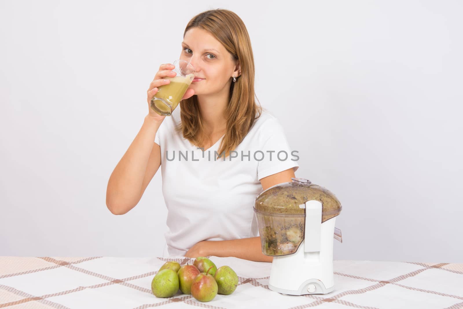 Young beautiful girl in the juicer squeezed pear juice and sitting at a table with a glass of juice in hand