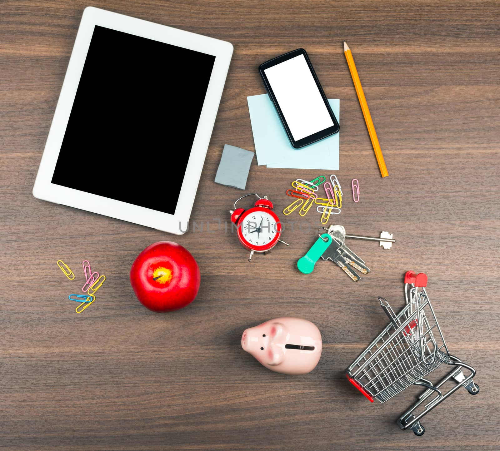 Shopping cart with office supplies and tablet on wooden table