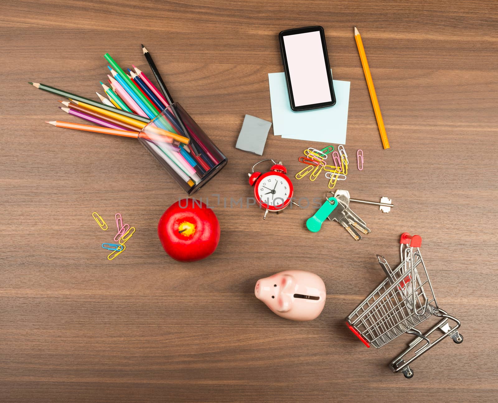 Shopping cart with office supplies and alarm clock on wooden table