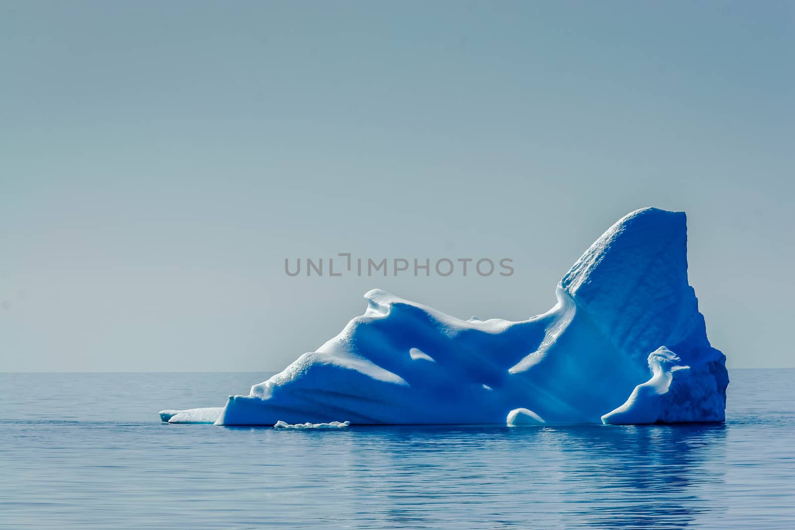 A melting deep blue iceberg waits in the Arctic Ocean