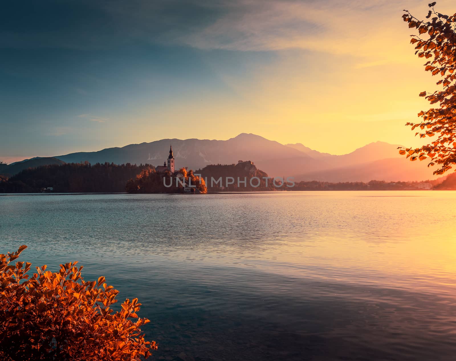 Famous Catholic Church on Little Island in Bled Lake, Slovenia at Autumn Sunrise with Mountains in Background