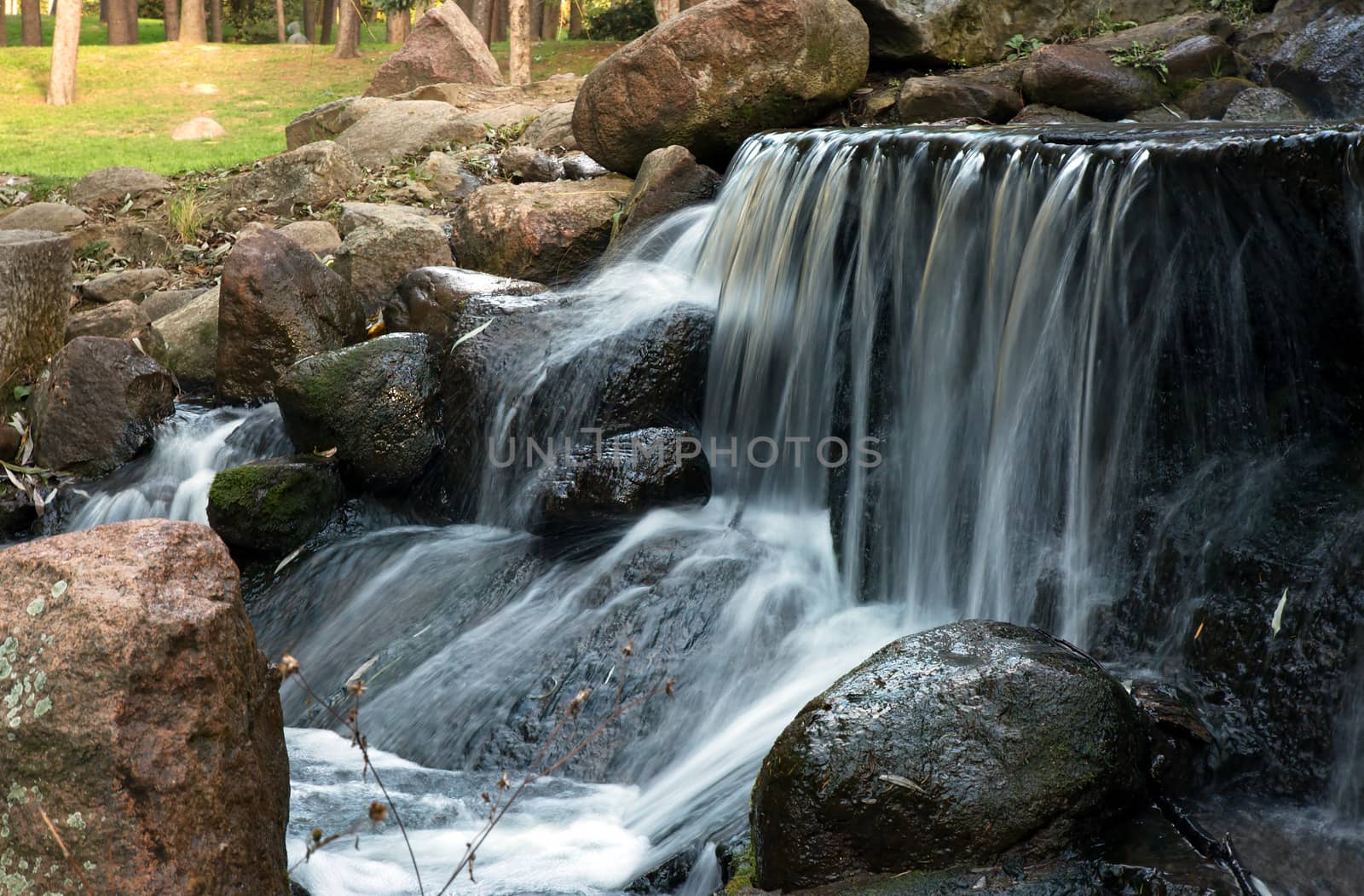 Poland.Park in Warsaw.Autumn.October.Small waterfall in the park.Ledge with the flow.Water falling from the top of the stones.Horizontal view.