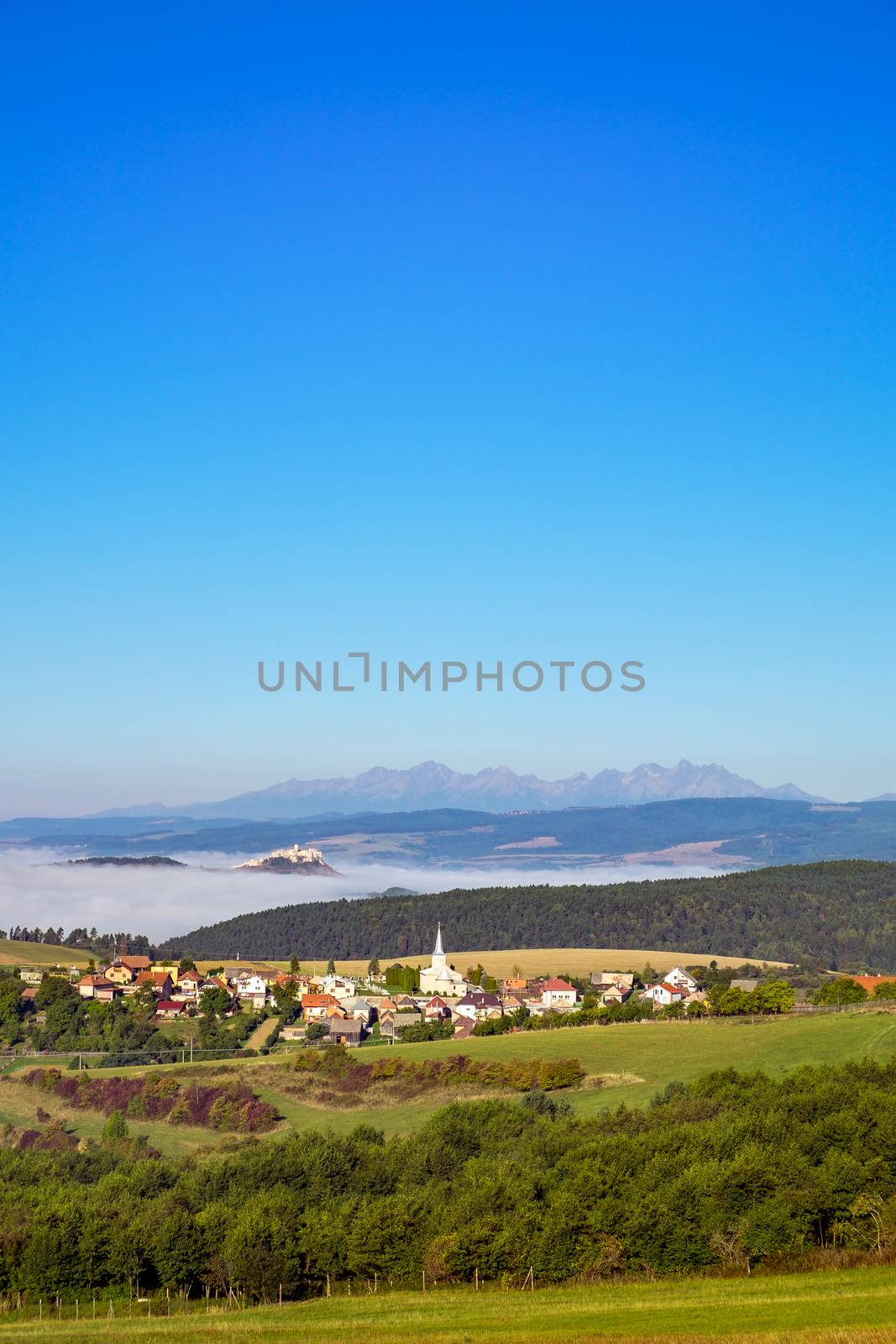 Scenic view of traditional village, Spis castle, meadows and High Tatras mountain range, Slovakia