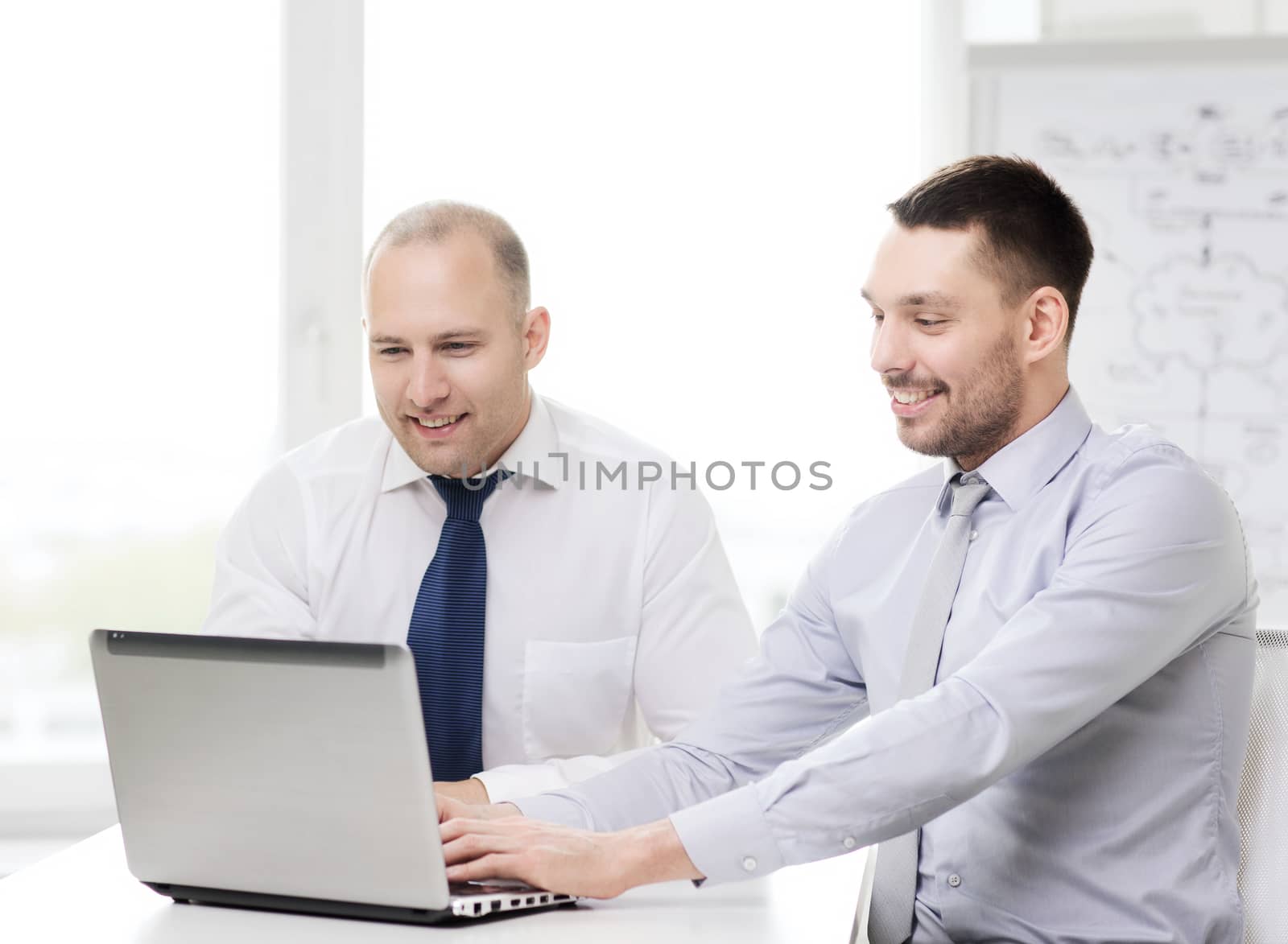 business, technology and office concept - two smiling businessmen with laptop in office