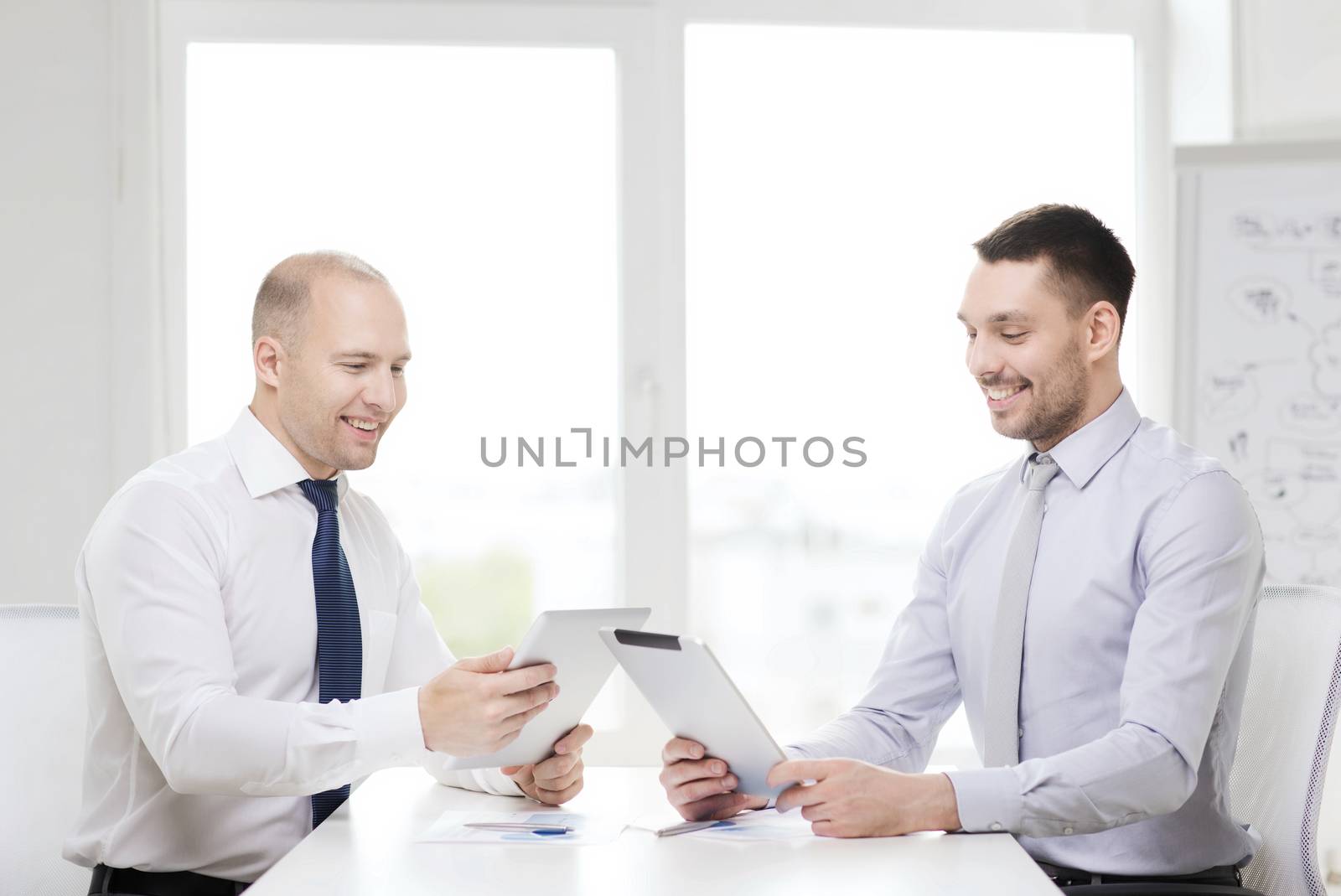 two smiling businessmen with tablet pc in office by dolgachov