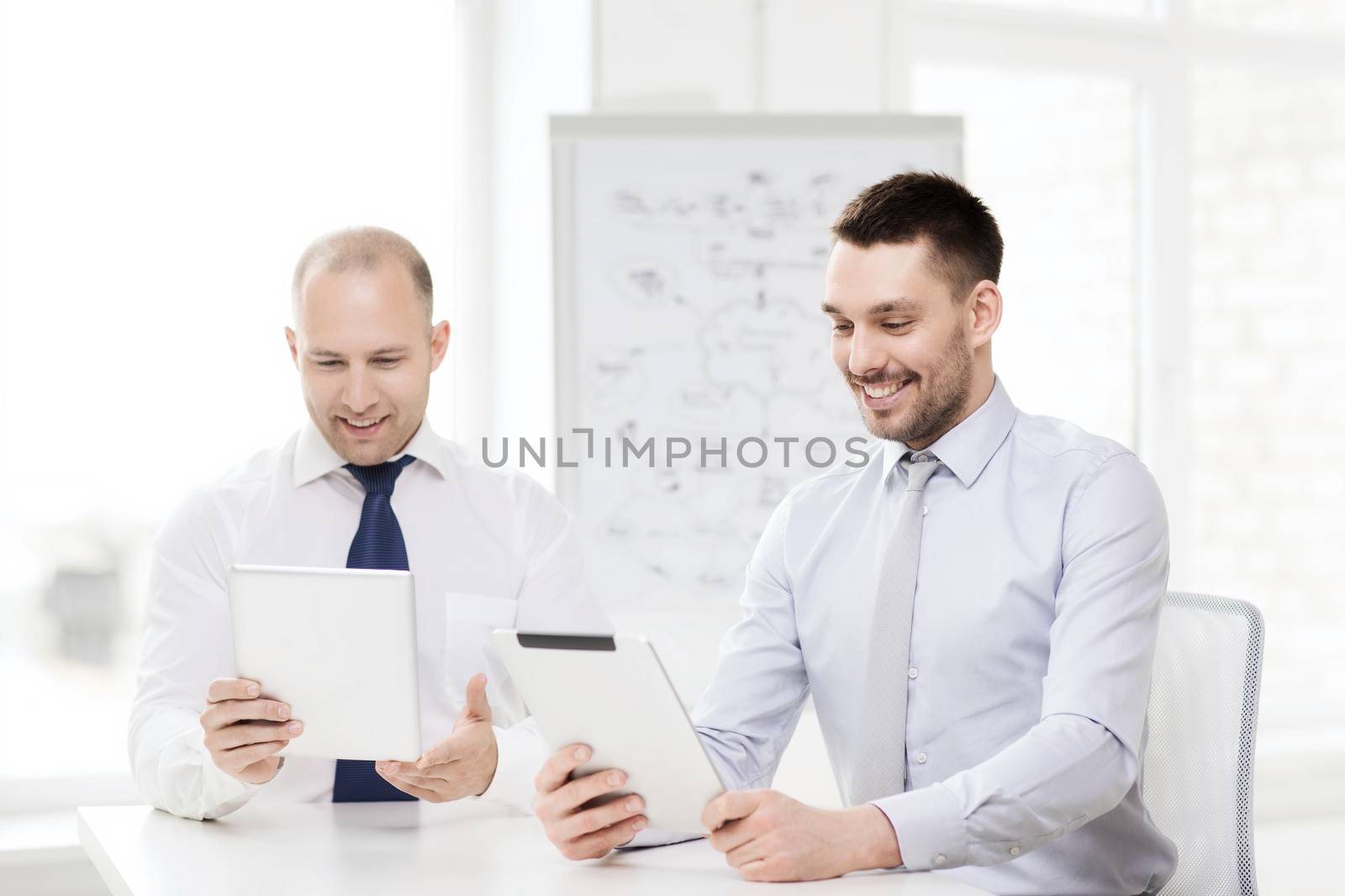 business, technology and office concept - two smiling businessmen with tablet pc computers in office