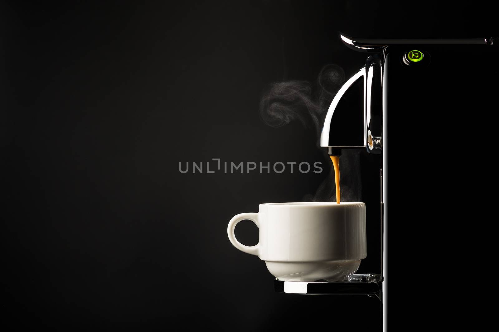 Preparing a cup of strong freshly brewed espresso coffee using a coffee machine with a side view of the beverage pouring into a white cup on a dark shadowy background