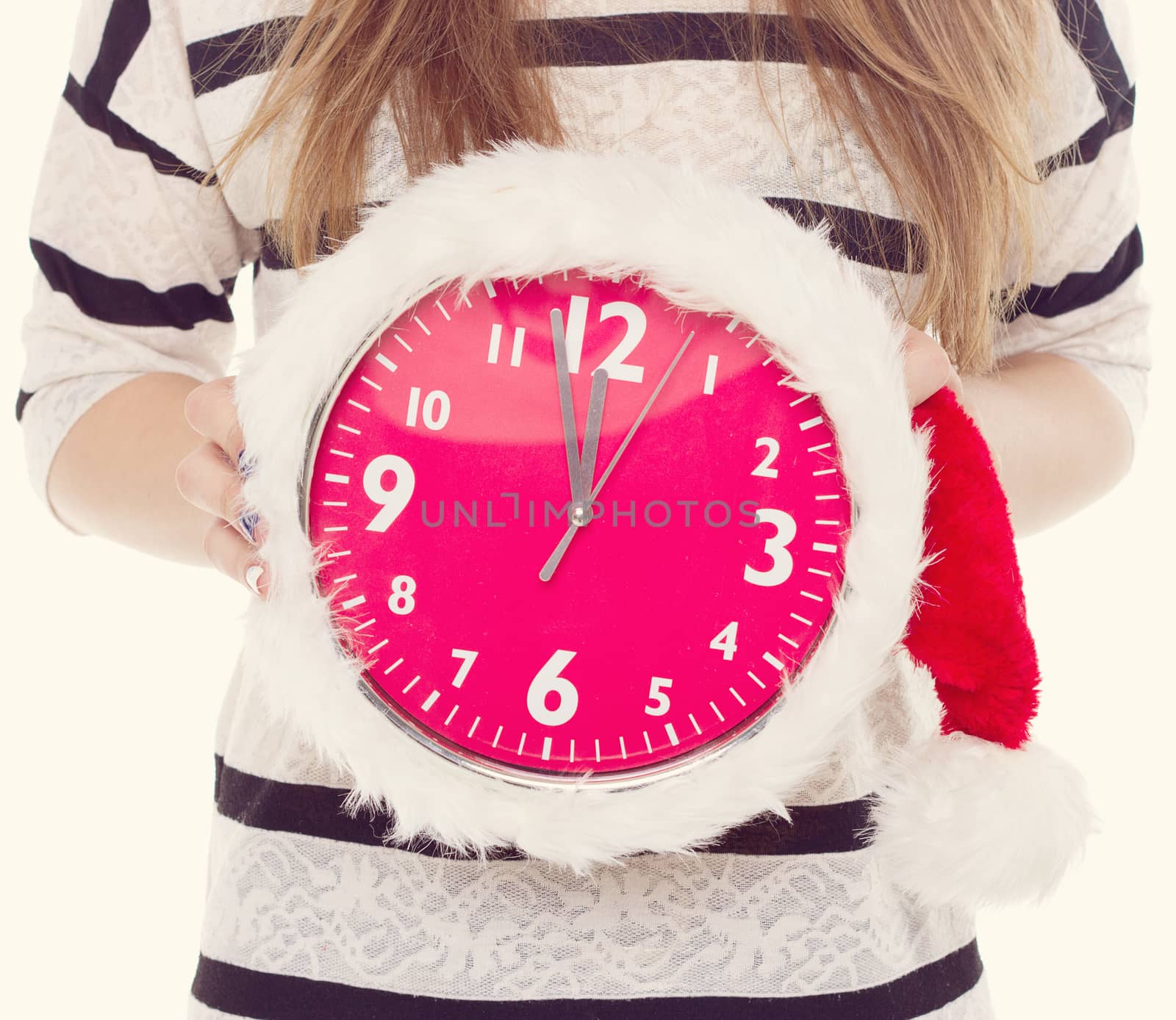 Big clocks in a Christmas hat in female hands. New Year. 12 hours. toning