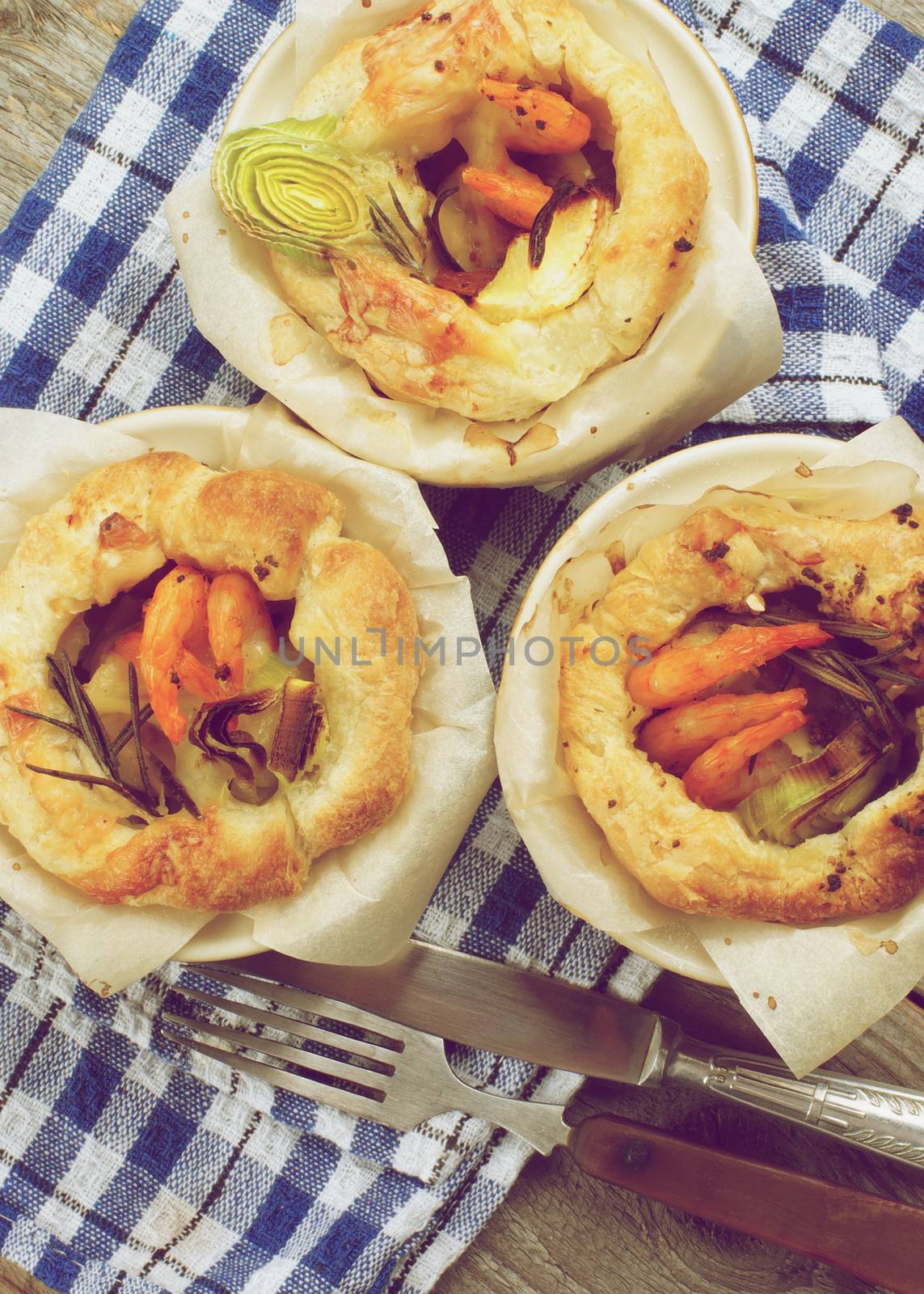 Delicious Puff Pastry Snacks with Shrimps, Leek and Cheese Oven-Baked in Ramekin with Fork and Knife on Checkered Napkin. Retro Styled
