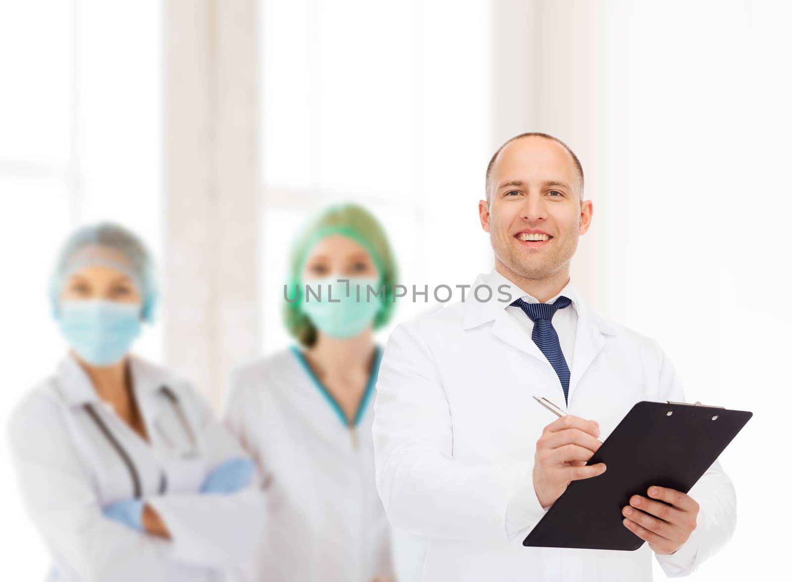 medicine, profession, teamwork and healthcare concept - smiling male doctor with clipboard writing prescription over group of medics