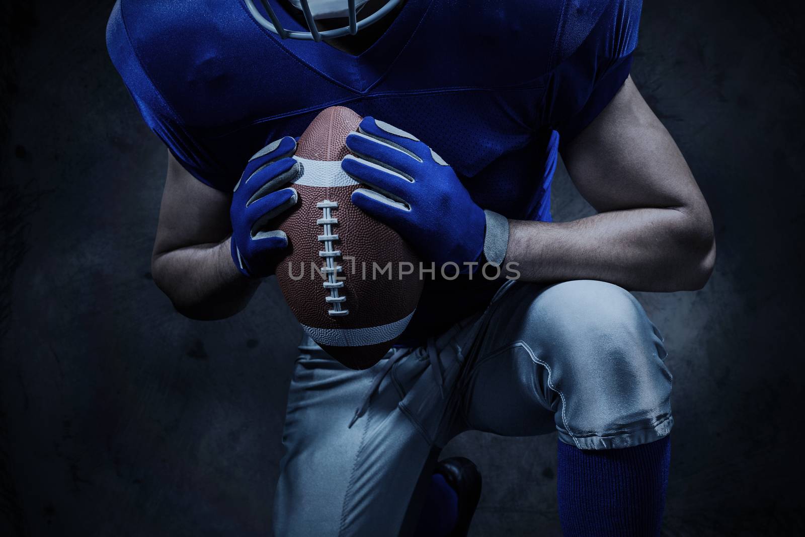 Mid section of American football player kneeling while holding ball against orange background