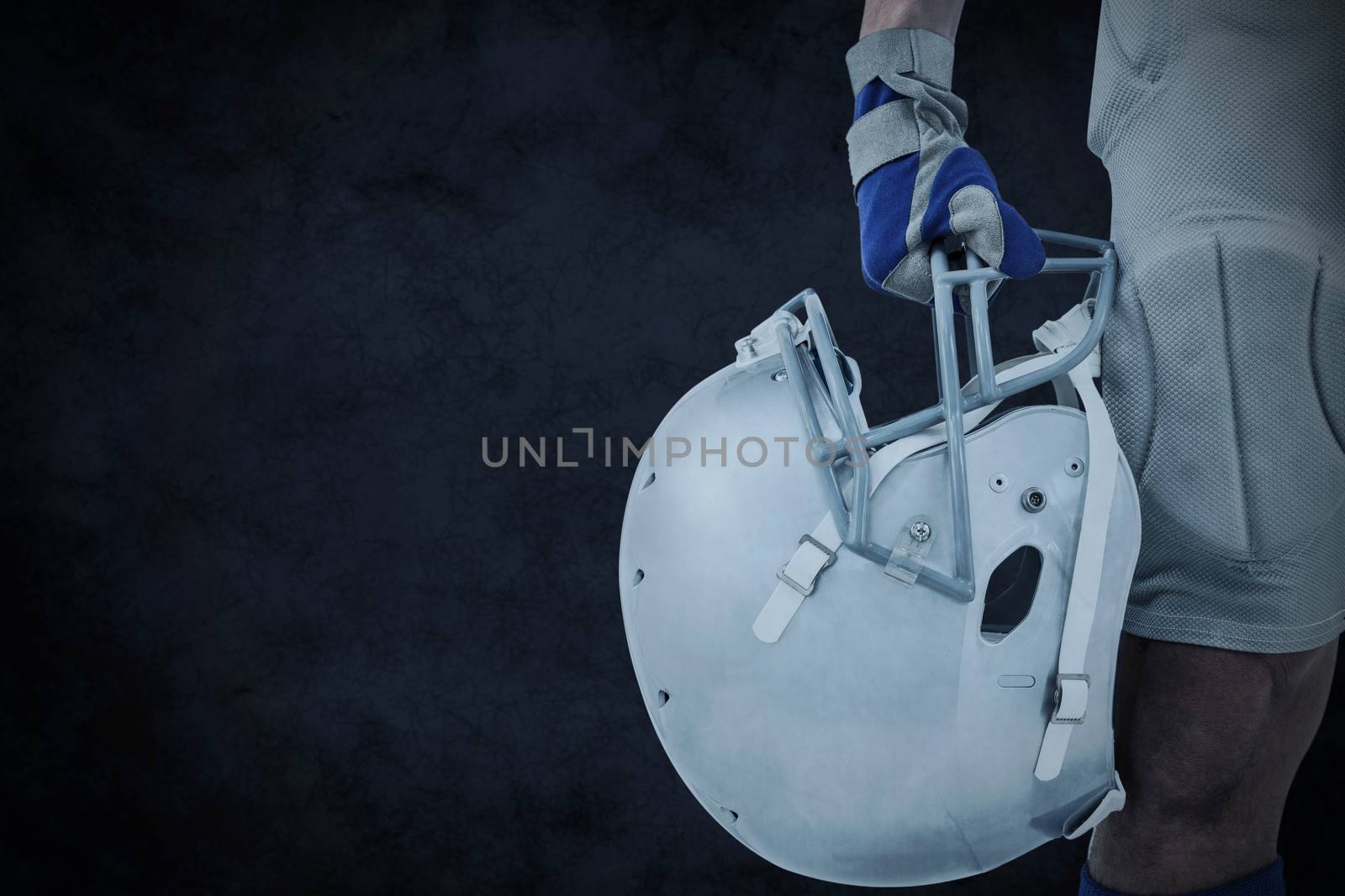 Close-up of American football player holding helmet against grey background