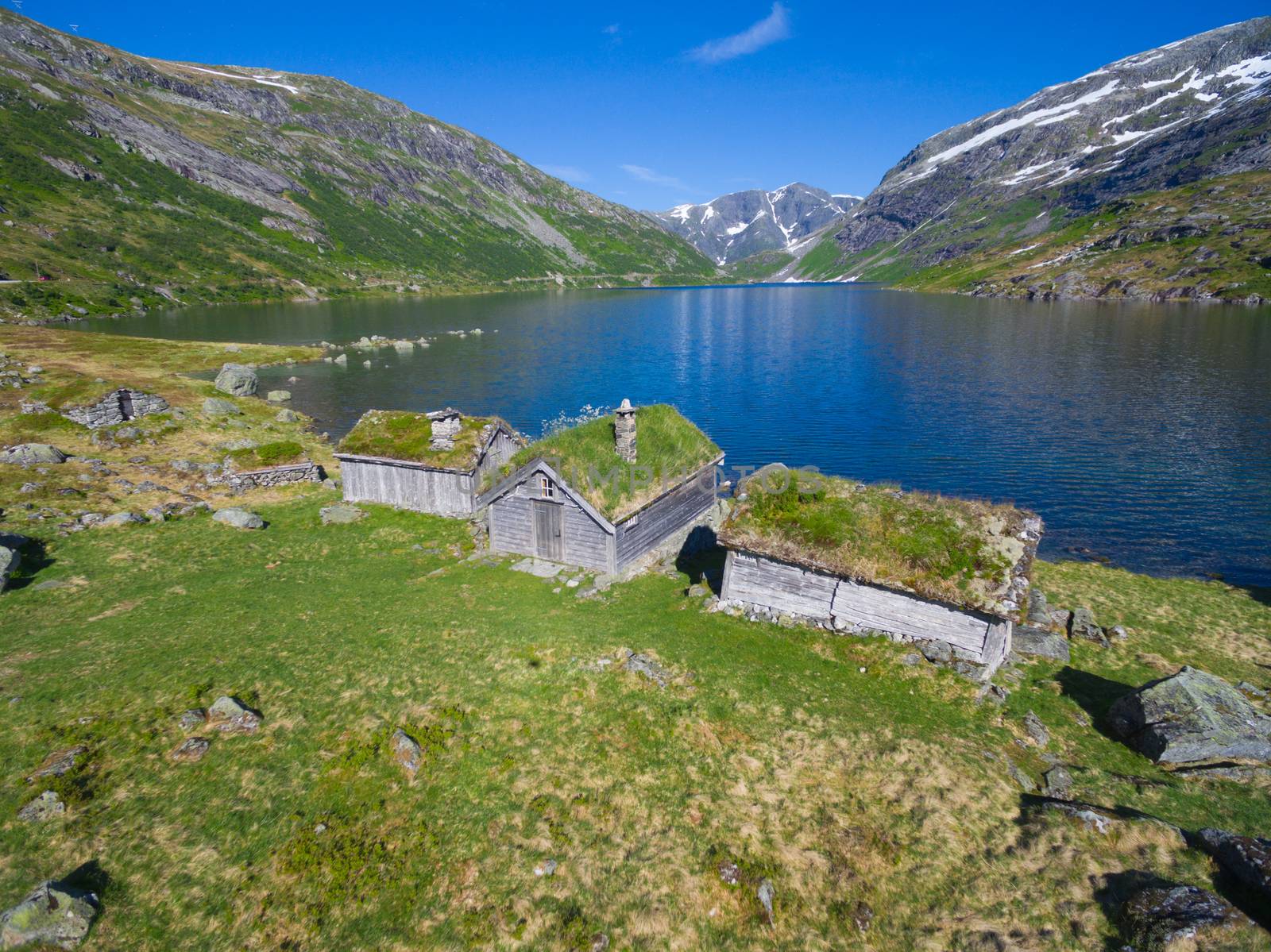 Aerial view of old norwegian huts by picturesque lake surrounded by mountains in Gaularfjellet mountain pass in Norway