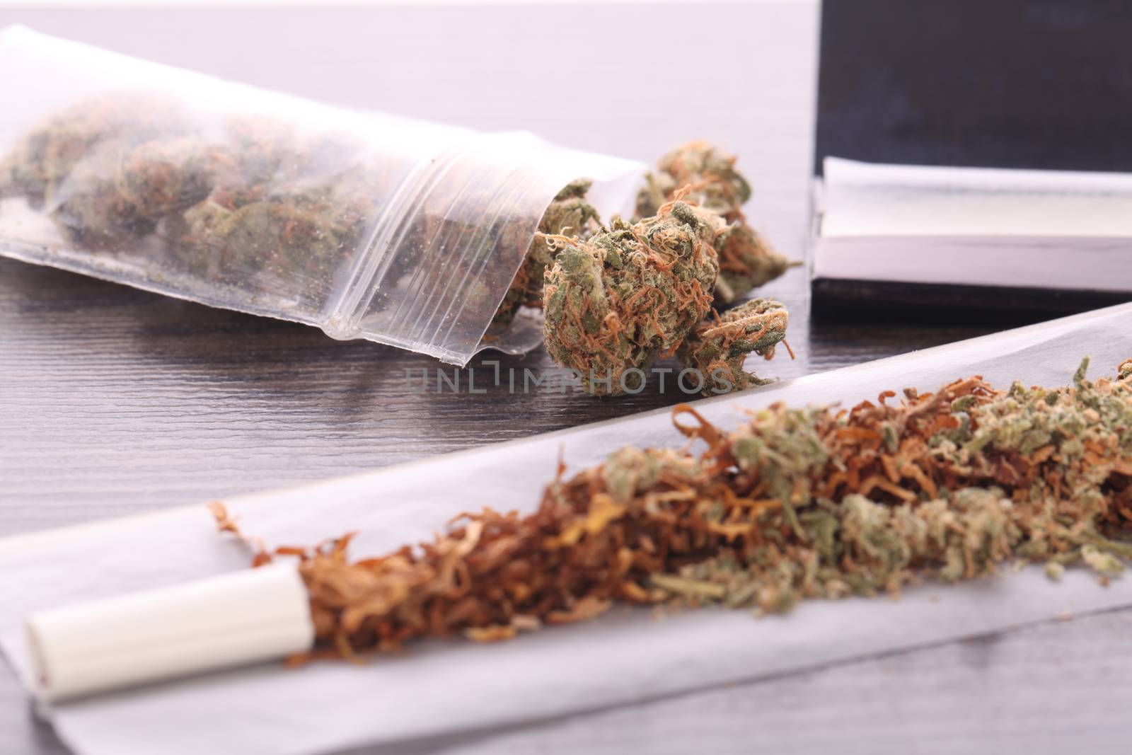 Close up Dried Cannabis Leaves on a Resealable Cellophane Wrapper and a Rolling Paper with Filter on Top of the Table