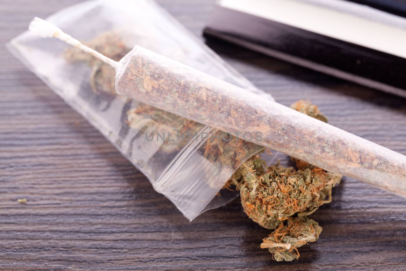 Close up Dried Cannabis Leaves on a Resealable Cellophane Wrapper and a Rolling Paper with Filter on Top of the Table