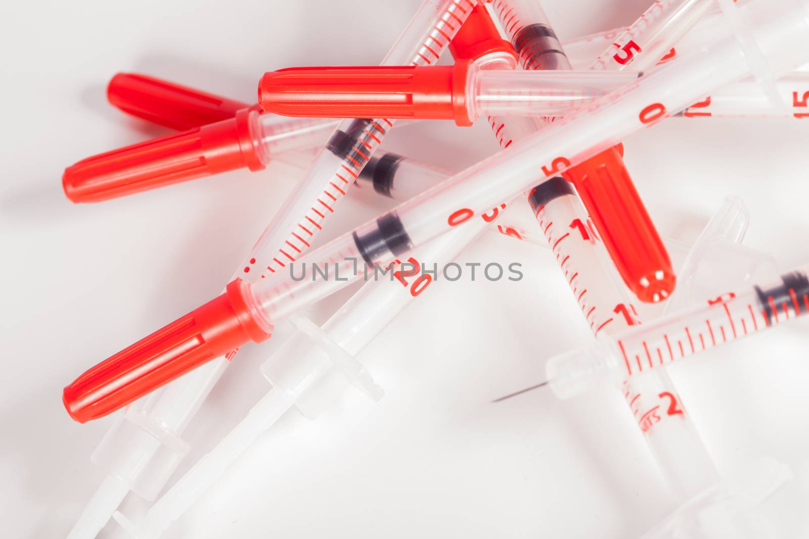 Still Life Close Up of Pile of Empty Syringe Needles with Red Safety Caps in Studio with White Background