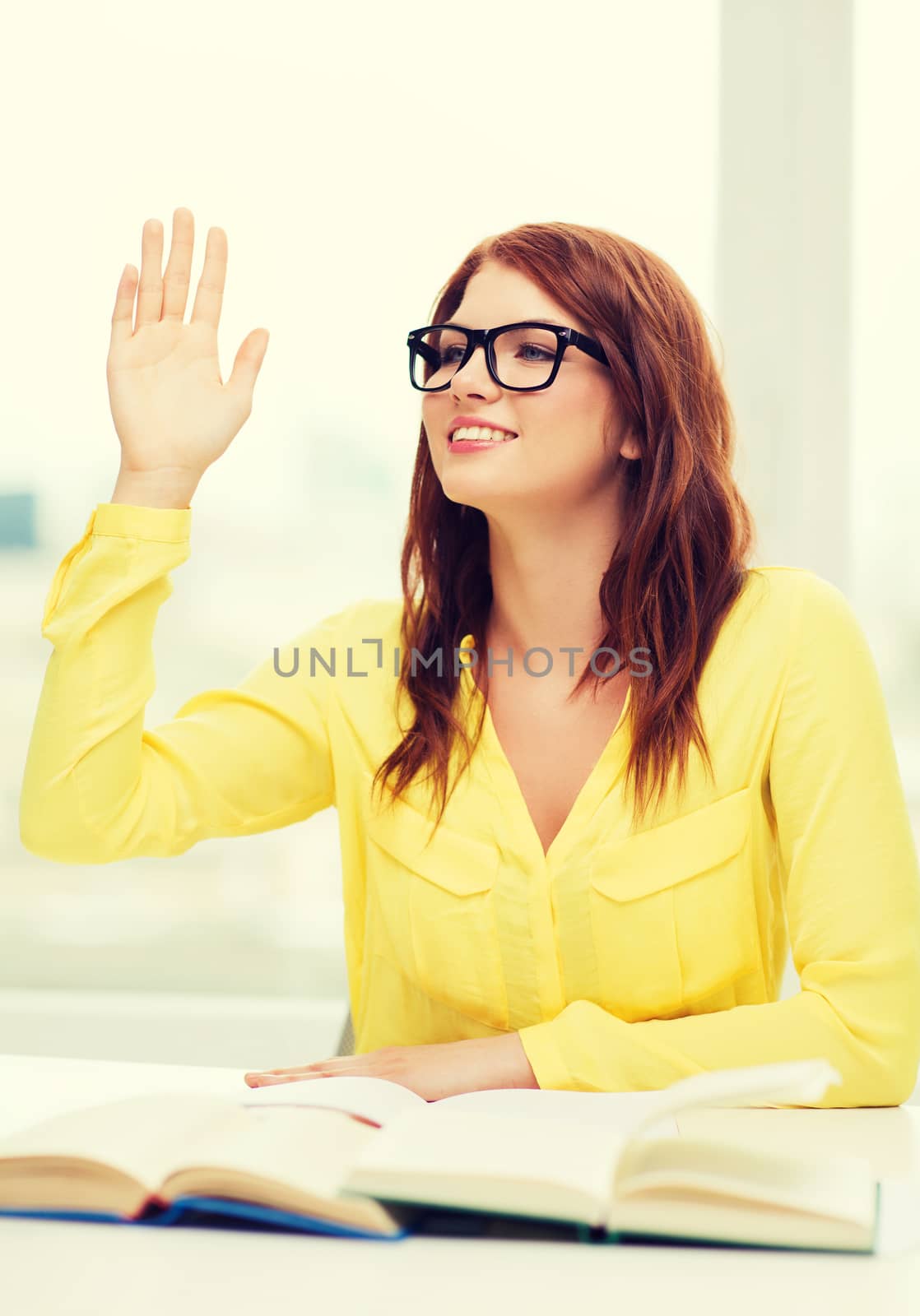 education concept - smiling student girl in eyeglasses with books and raised hand in college