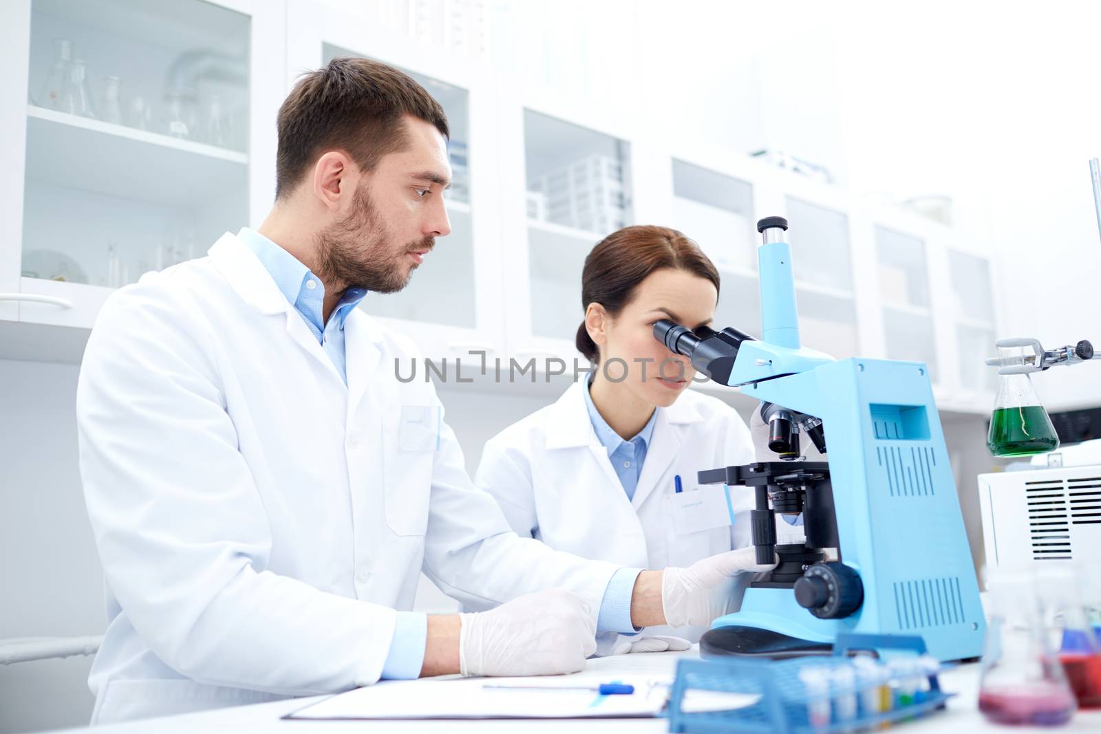 scientists with clipboard and microscope in lab by dolgachov