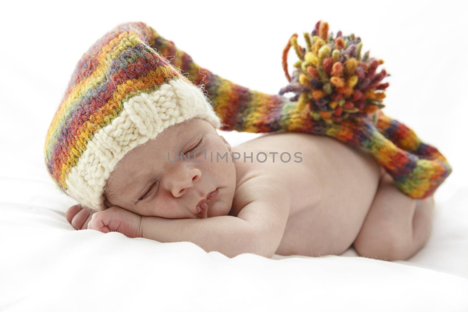 Sleeping newborn baby wearing a long multicolor hat.