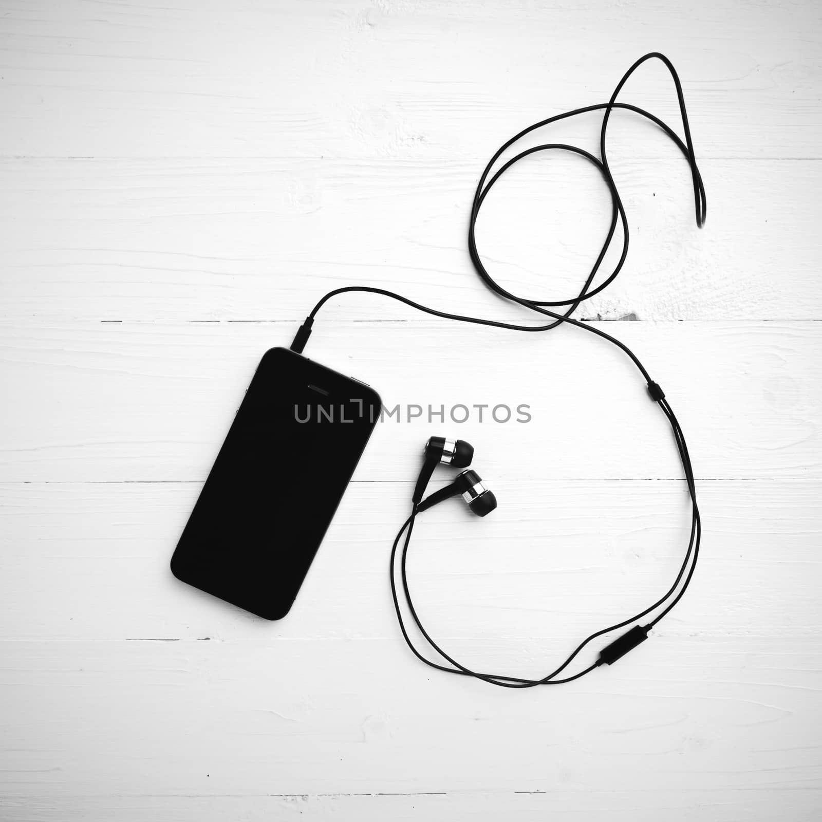cellphone with earphone over white table black and white color tone style