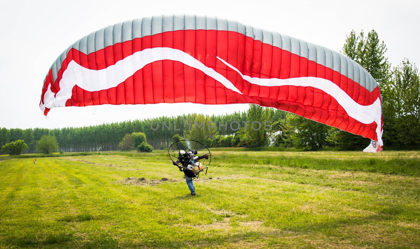 man with red motorized paraglider takes off from a green field