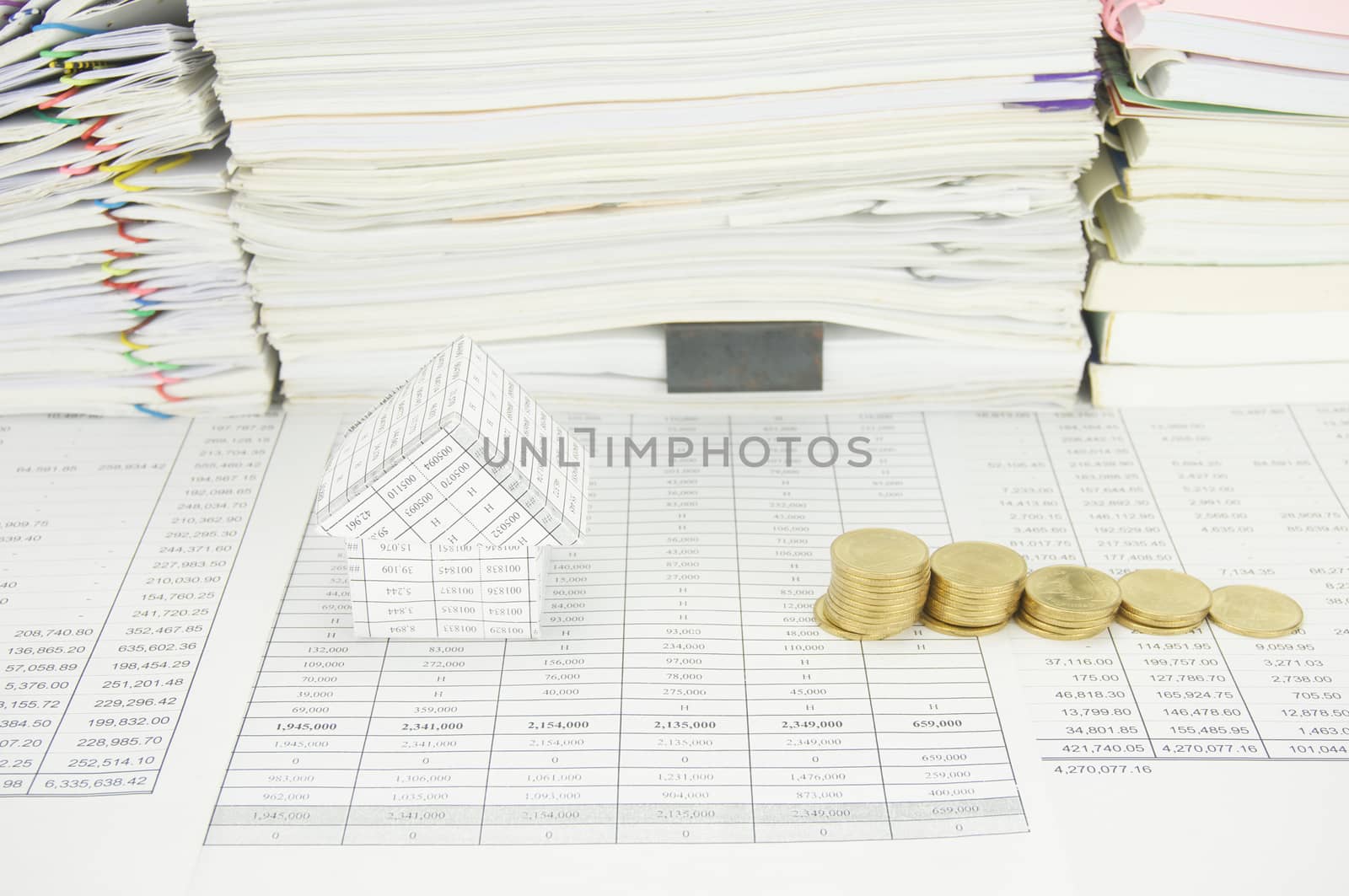 House and step pile of gold coins on finance account have paper of report and paperwork with books as background.