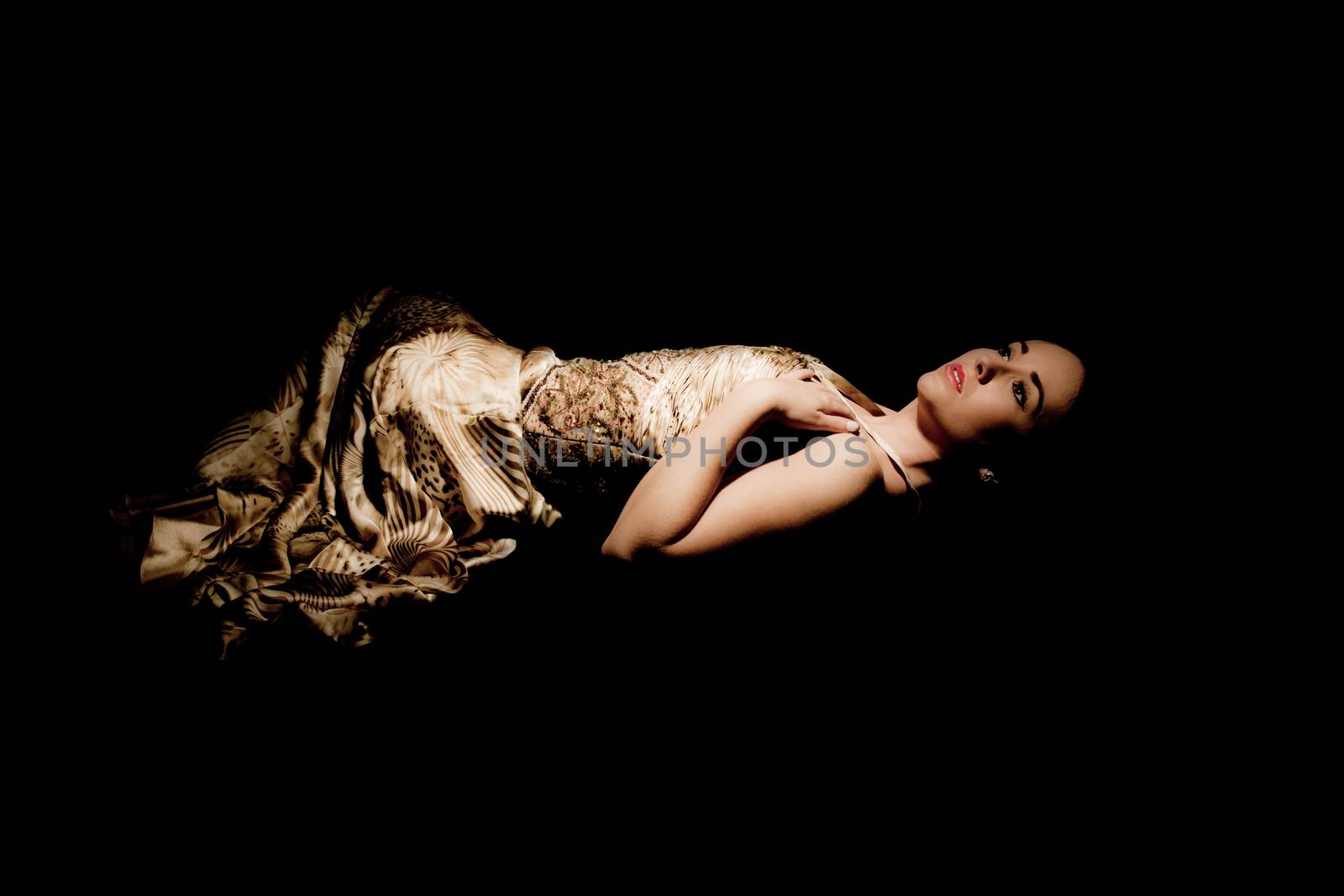 brunette woman in evening gown lying down on black background