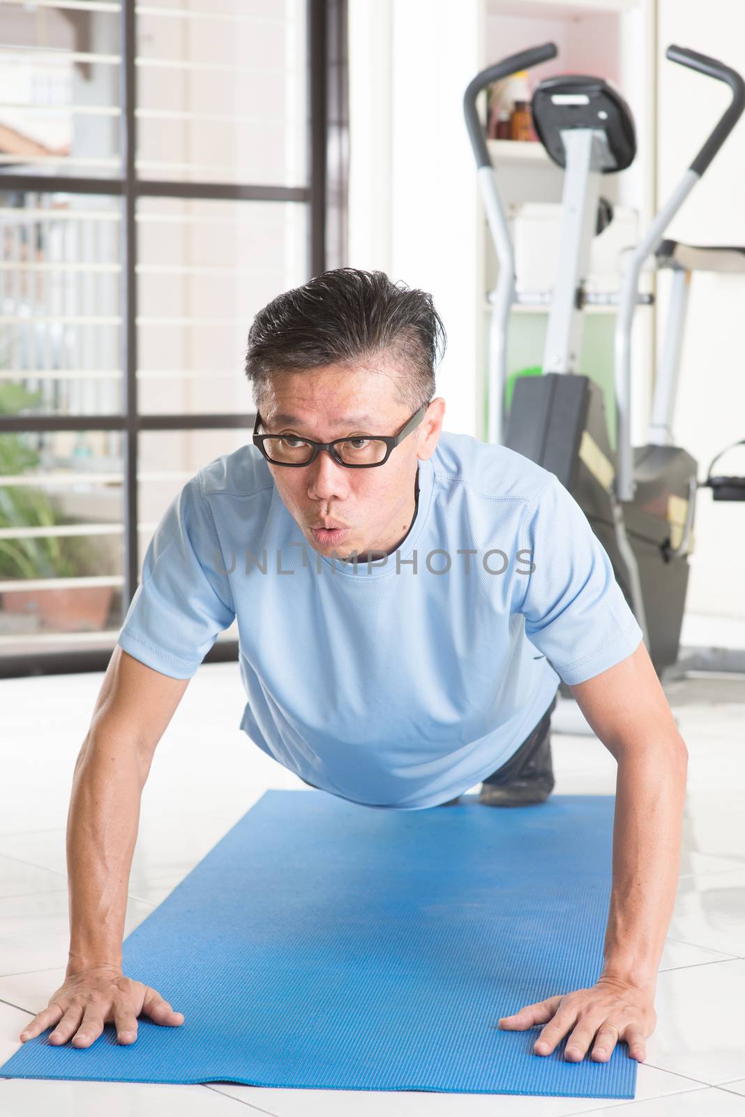 Portrait of active 50s mature Asian man in sportswear doing pushup on exercise mat, workout at indoor gym room.