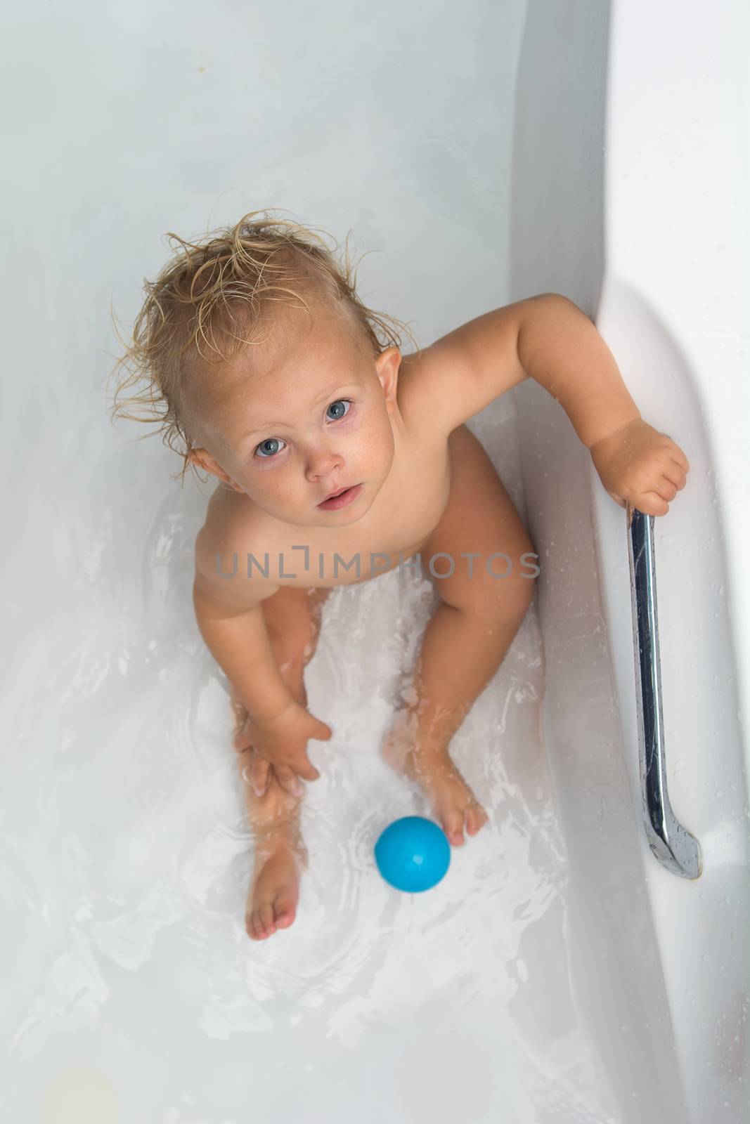 Baby sitting in water in a bath and playing with colourful balls. Close portrait.