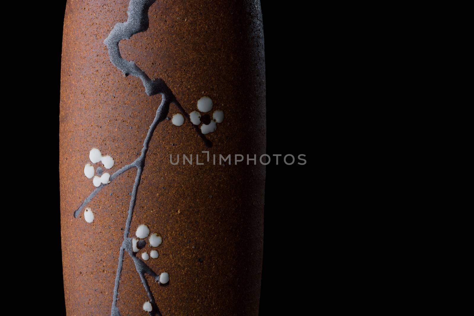 A Japanese vase painted with a branch from a cherry blossom tree dramatically lit and isolated on a black background.