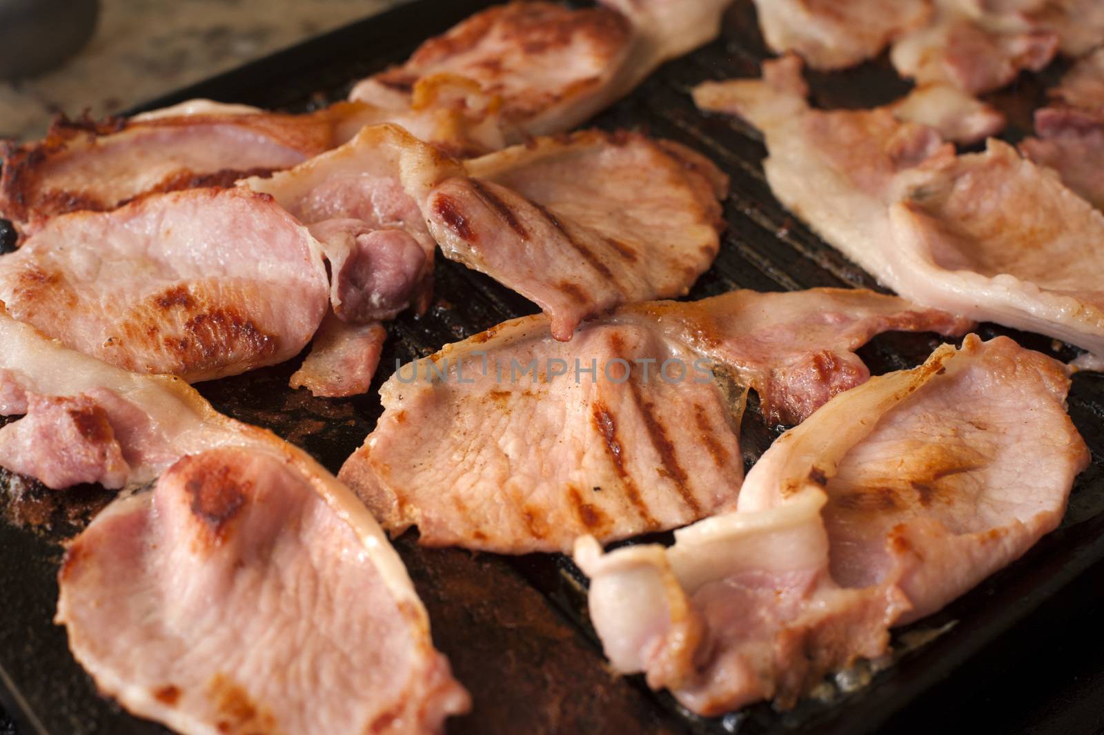 Cooking rashers of bacon for breakfast with a close up view of slices sizzling in a frying pan