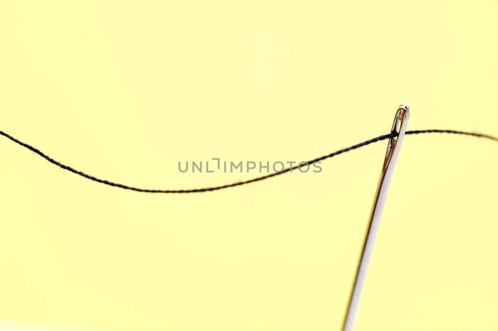 Threaded sewing needle with yarn over a yellow background with copyspace conceptual of sewing, needlework, tailoring or a seamstress