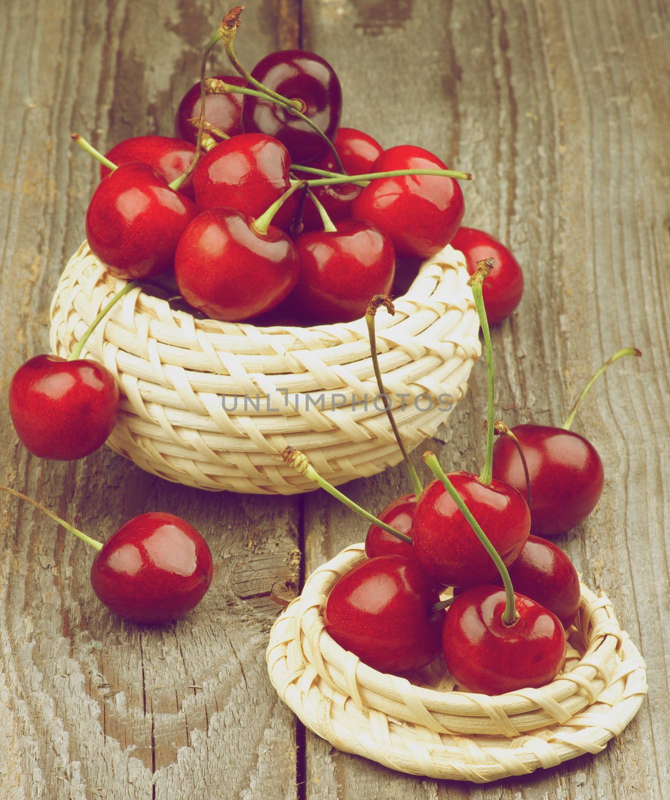 Two Wicker Bowls with Ripe Sweet Cherries isolated on Rustic Wooden background. Retro Styled