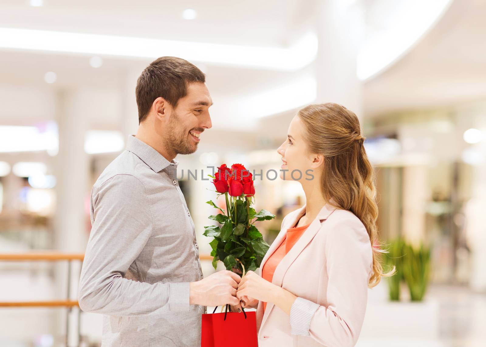 relations, love, romance and people concept - happy young couple with flowers talking in mall