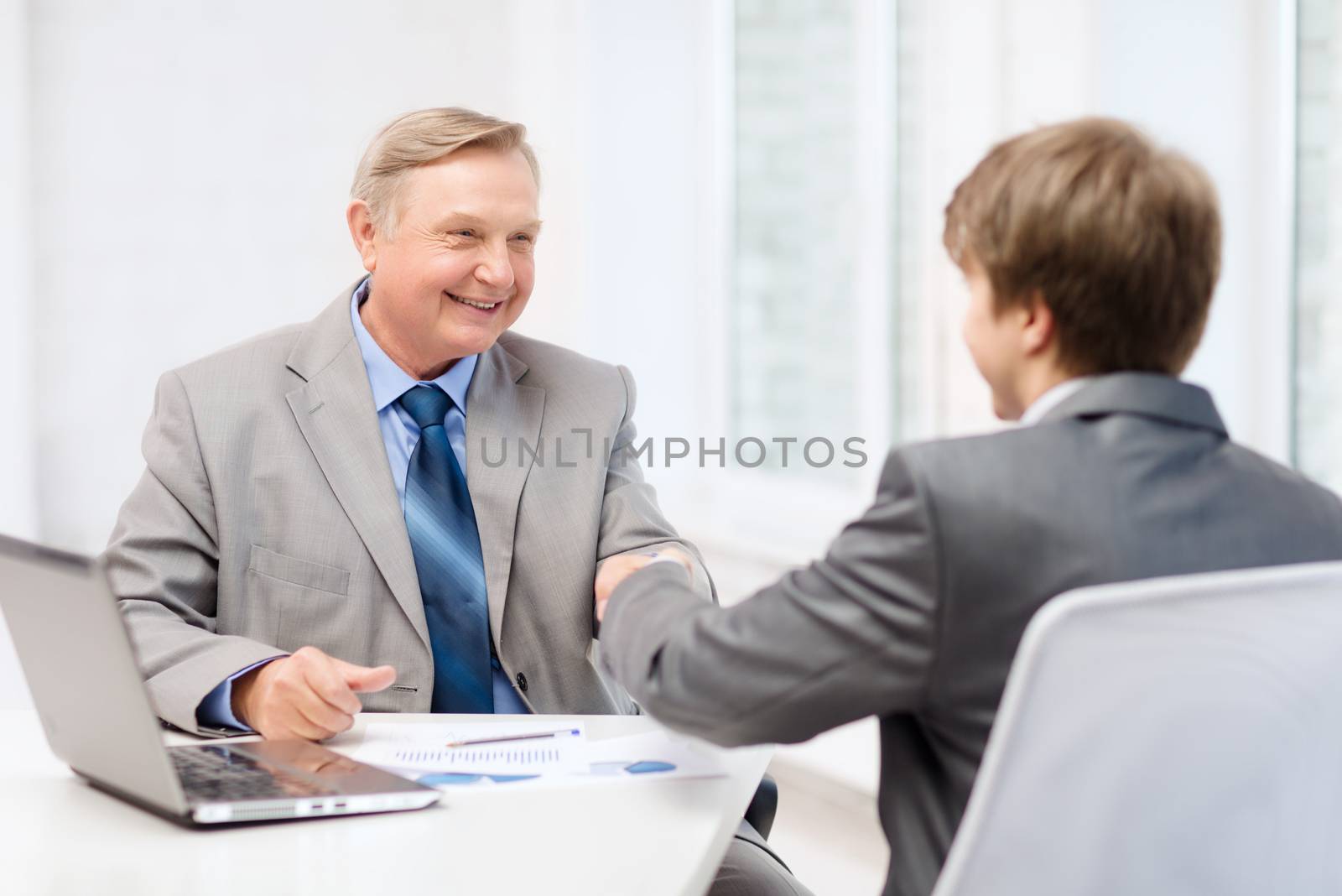 older man and young man shaking hands in office by dolgachov