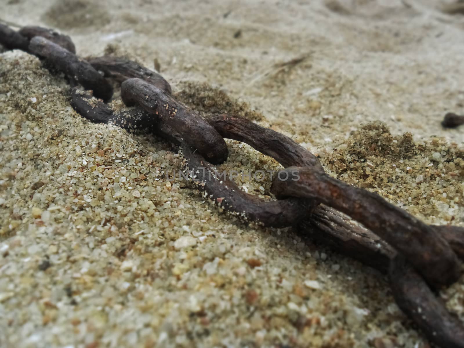 a rusted chain lying on light beach sand