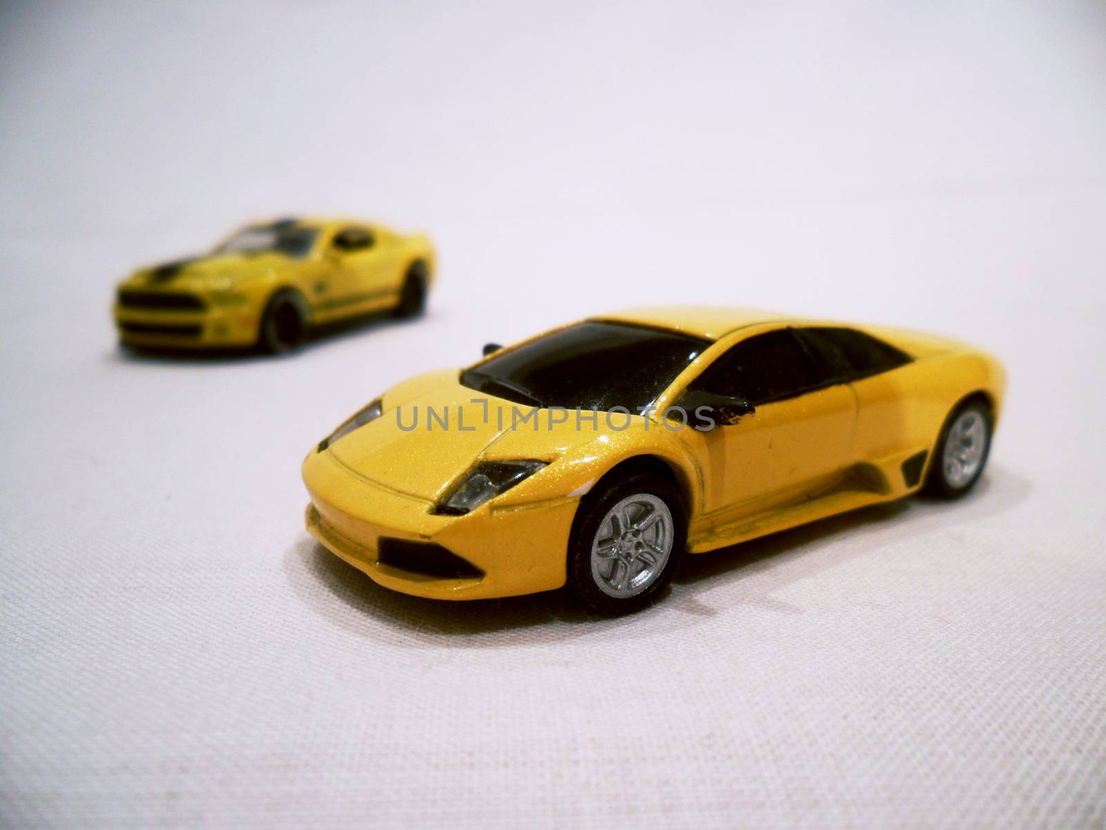 two yellow toy sports cars next to eachother on white sheet