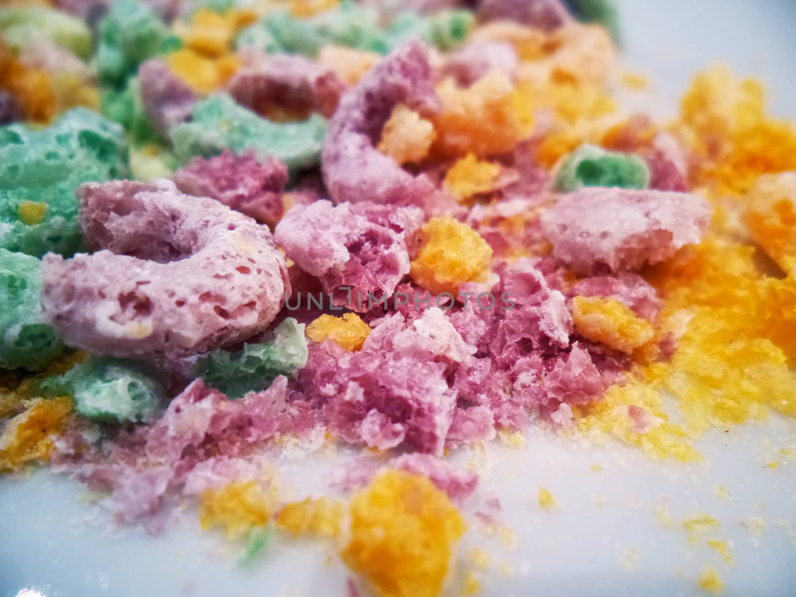 Close up of crushed up sugar coated colorful ceareal loops on white plate or surface