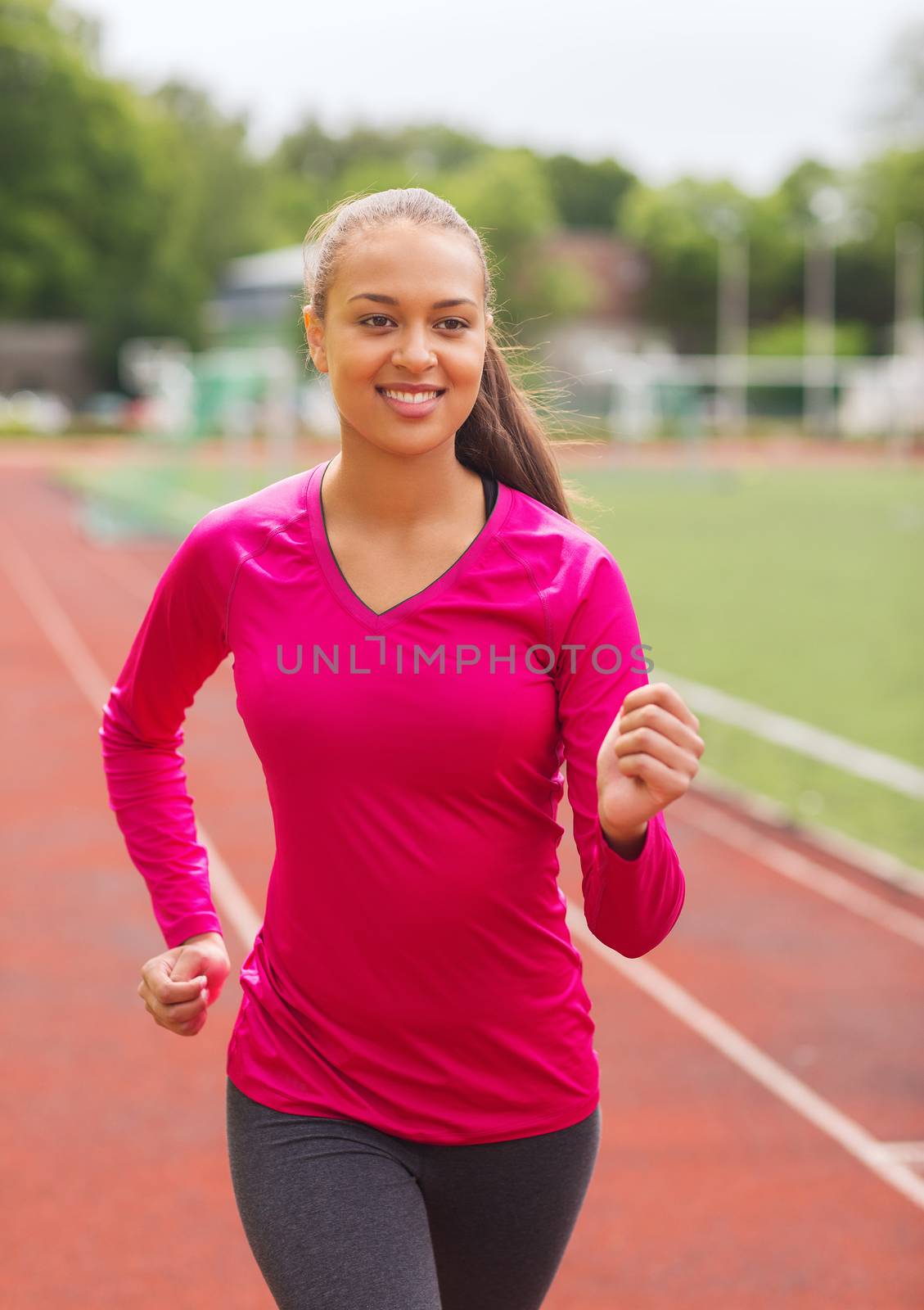 smiling young woman running on track outdoors by dolgachov