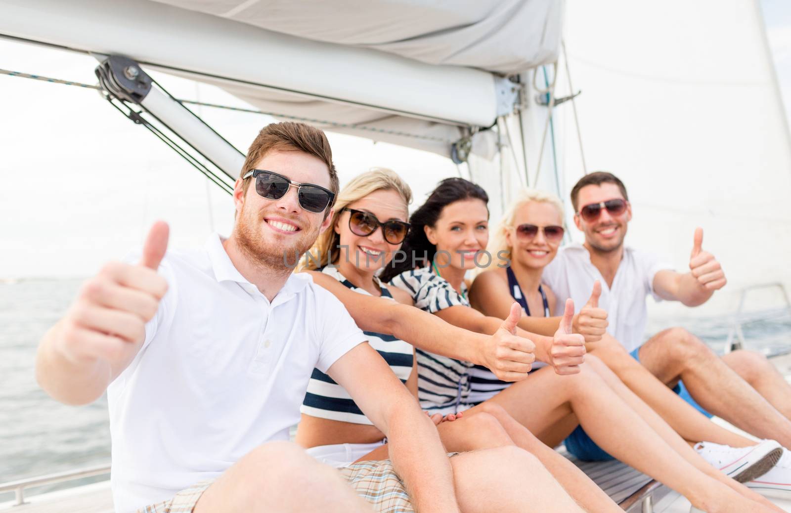 travel, sea, friendship, gesture and people concept - smiling friends sitting on yacht deck and showing thumbs up