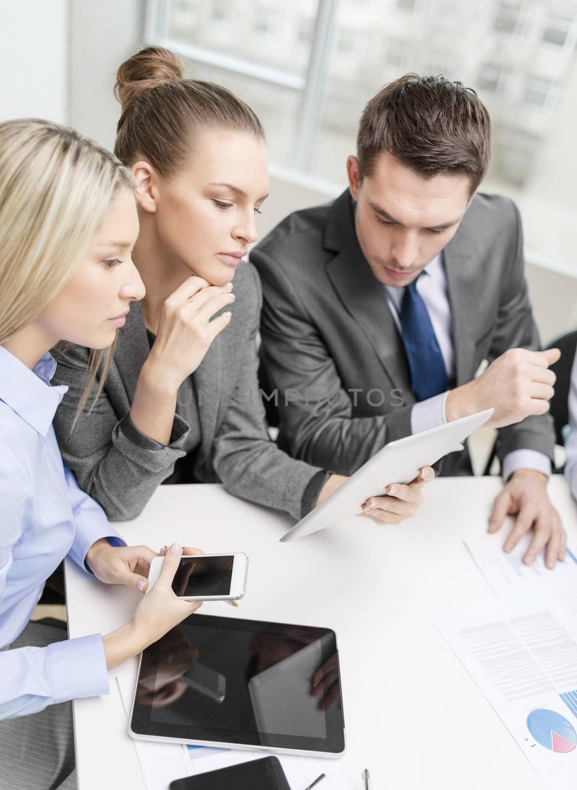 business, technology and office concept - serious business team with tablet pc, documents and smartphones having discussion in office