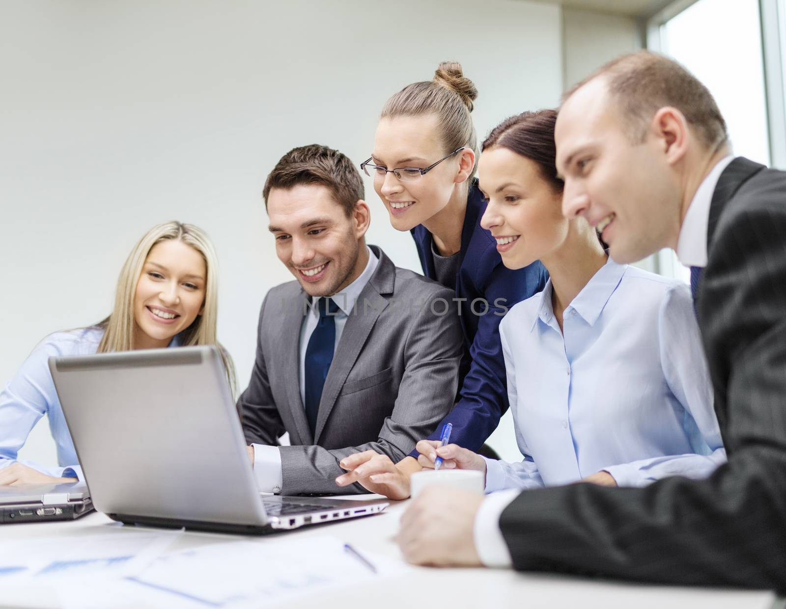 business, technology and office concept - smiling business team with laptop computers, documents and coffee having discussion in office