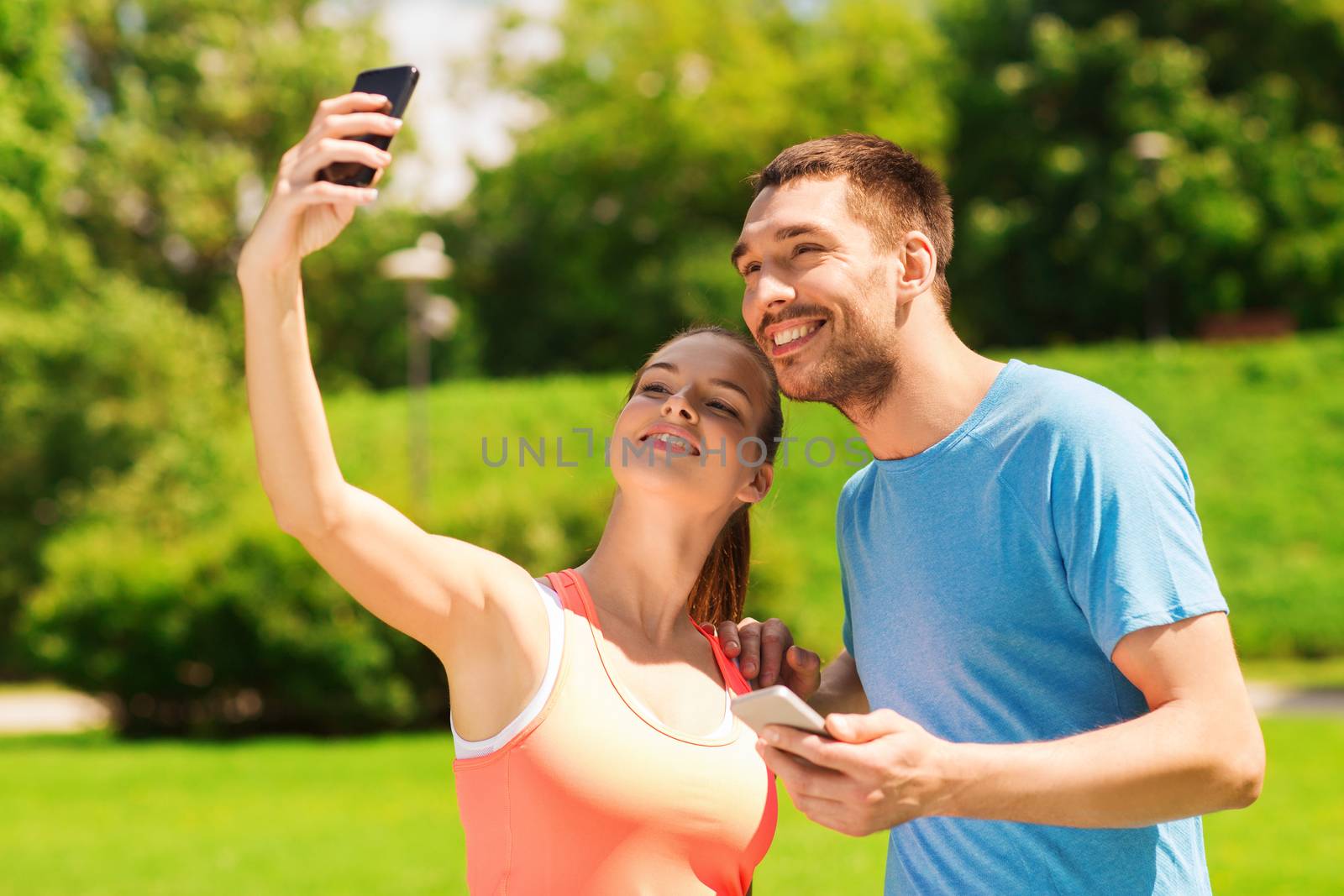 fitness, sport, training, technology and lifestyle concept - two smiling people with smartphones outdoors